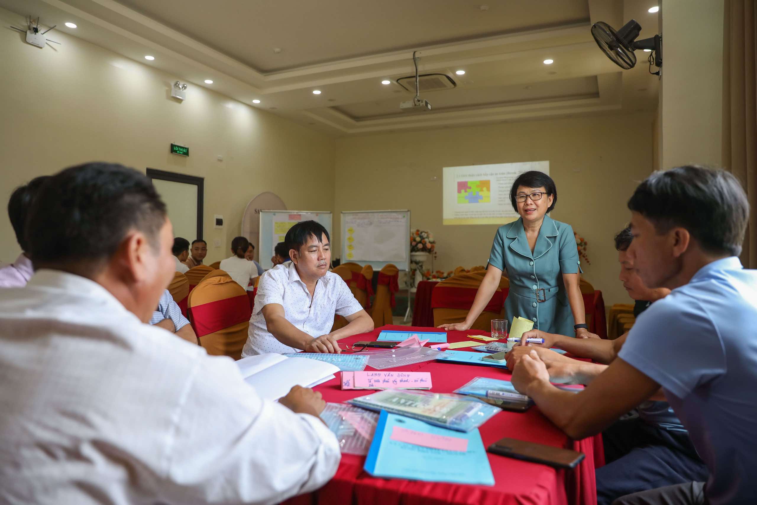 A group of academics sat around a red-clothed table covered in papers, presentation on the wall behind