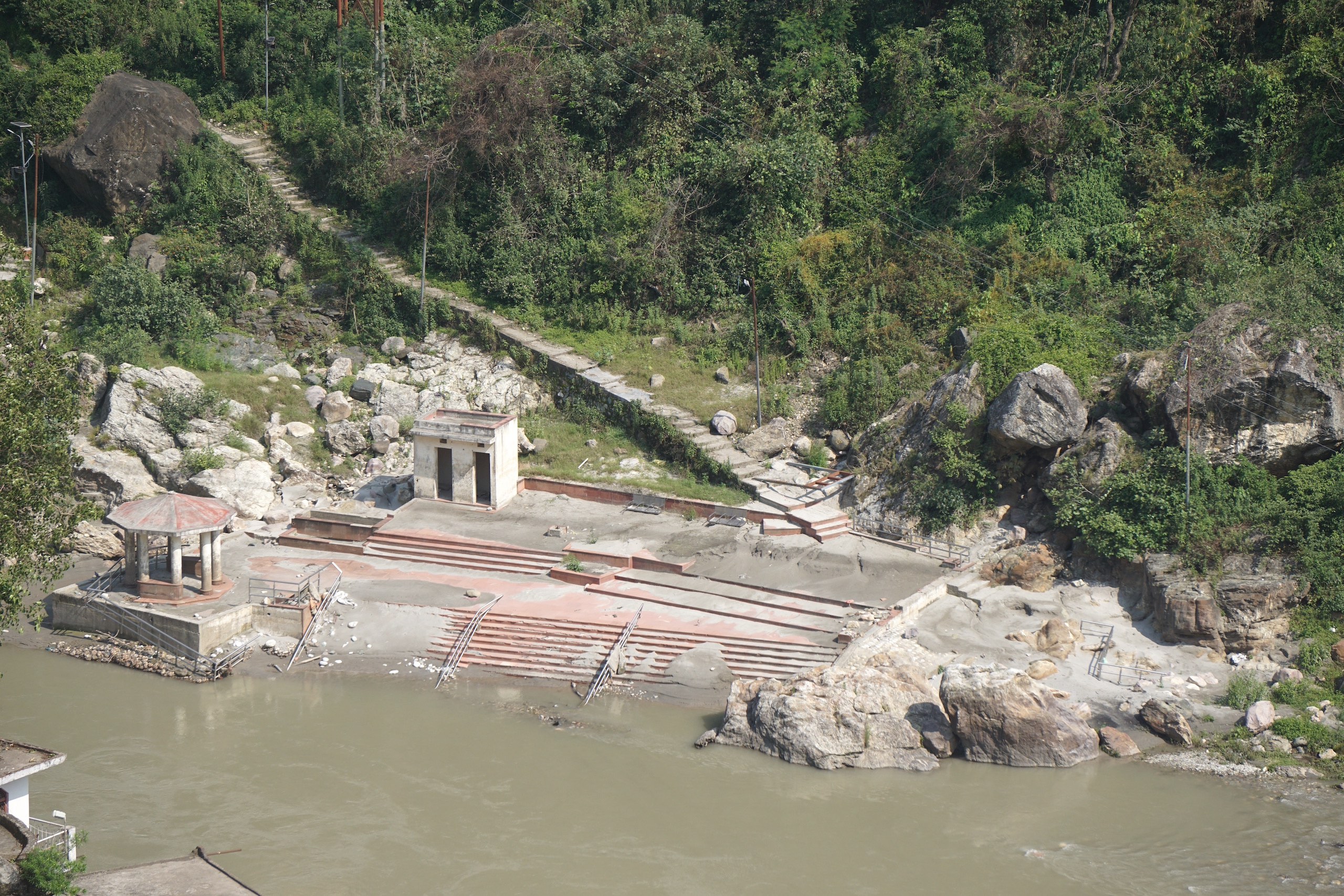a forested riverbank, a small building and steps down to the water