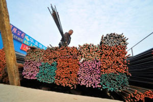 A labourer stands on a pile of colourful steel rods