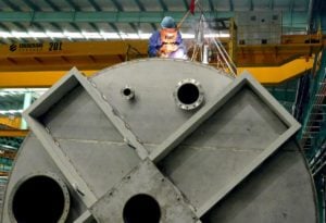 Person wearing visor welds steel atop a large metal cylinder