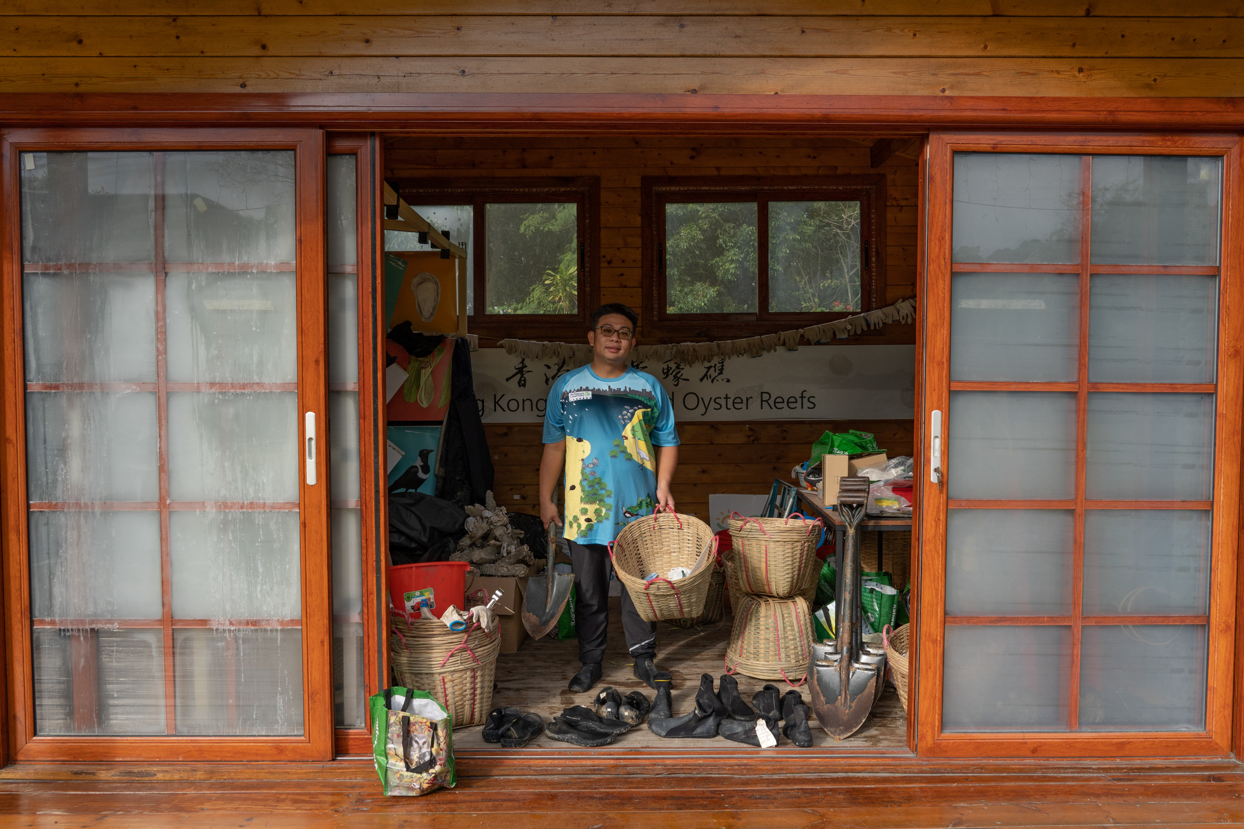 A man stands in the open doorway of a cluttered shed, holding a wicker basket