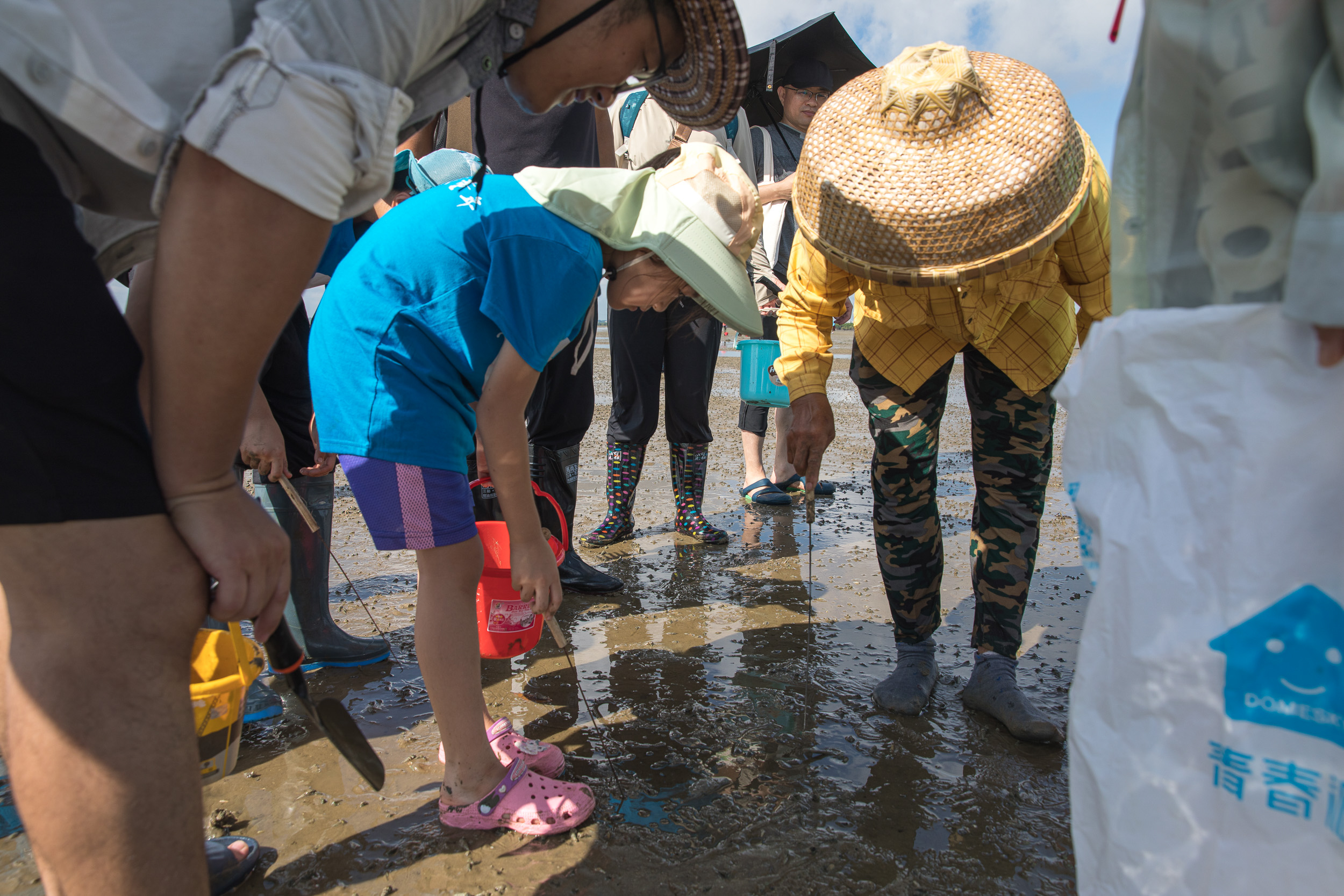 a group of people stand in a circle on a beach looking at the sand