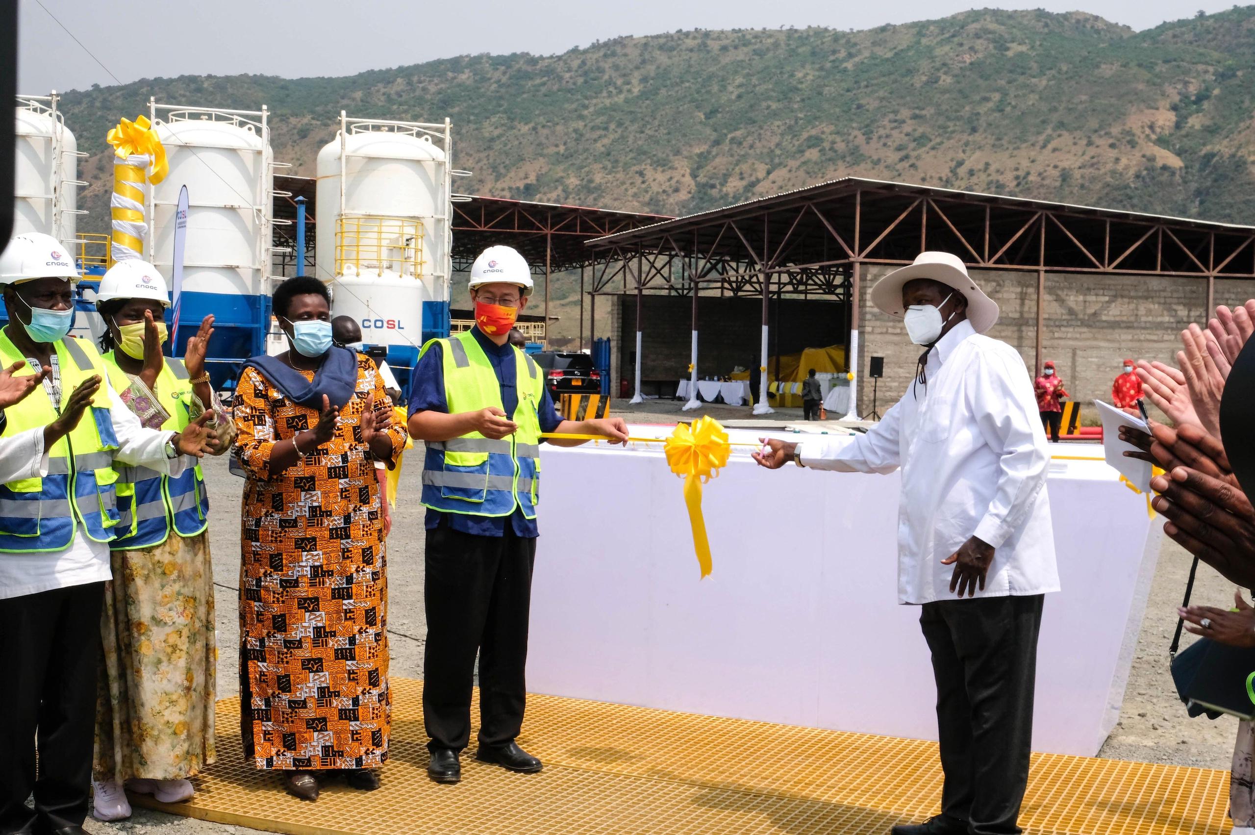People wearing facemasks cut a ribbon in front of an industrial facility, green hills in the background