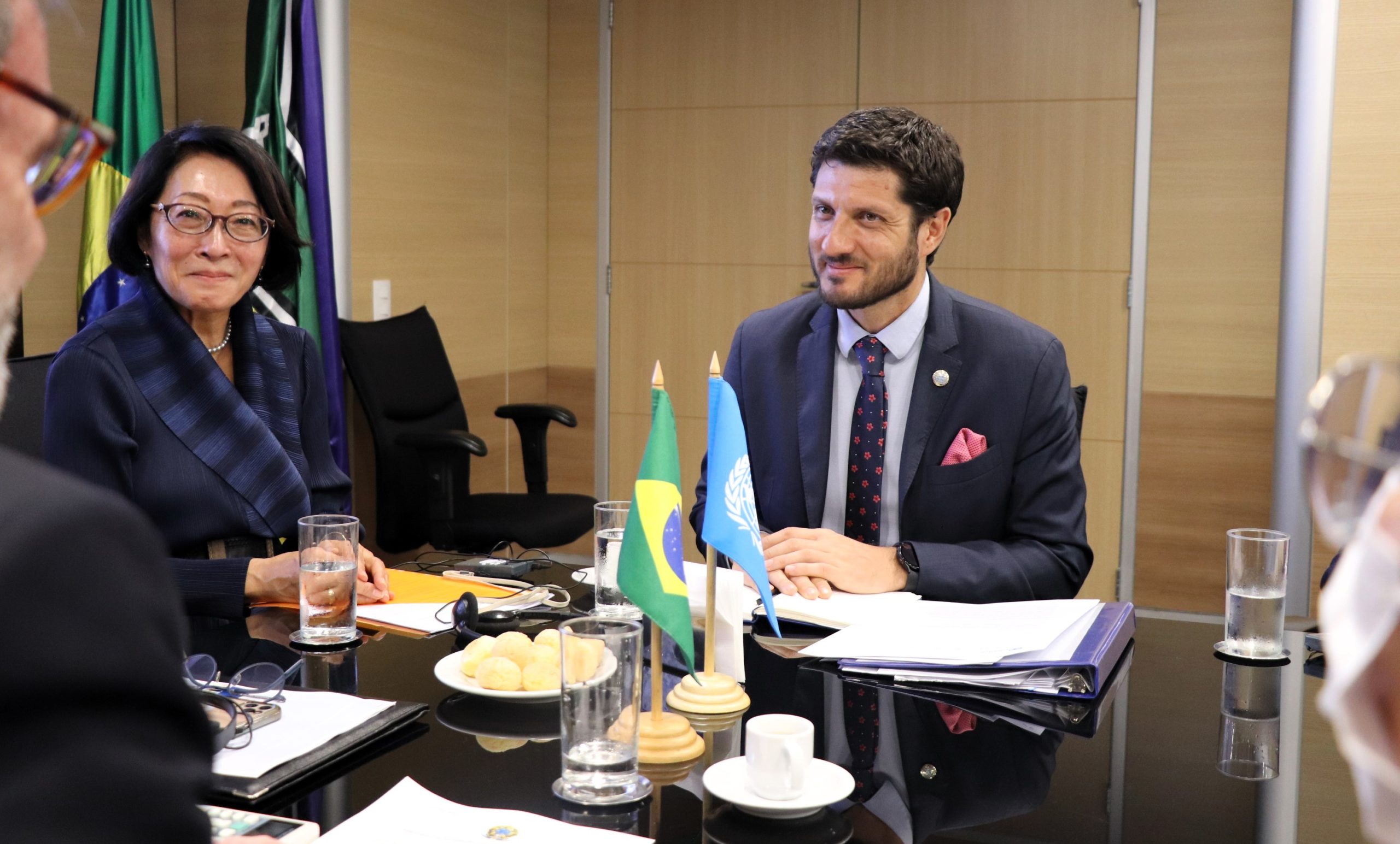Nahuel Arenas García y Mami Mizutori sentados en un amesa con banderas de Brasil y Naciones Unidas