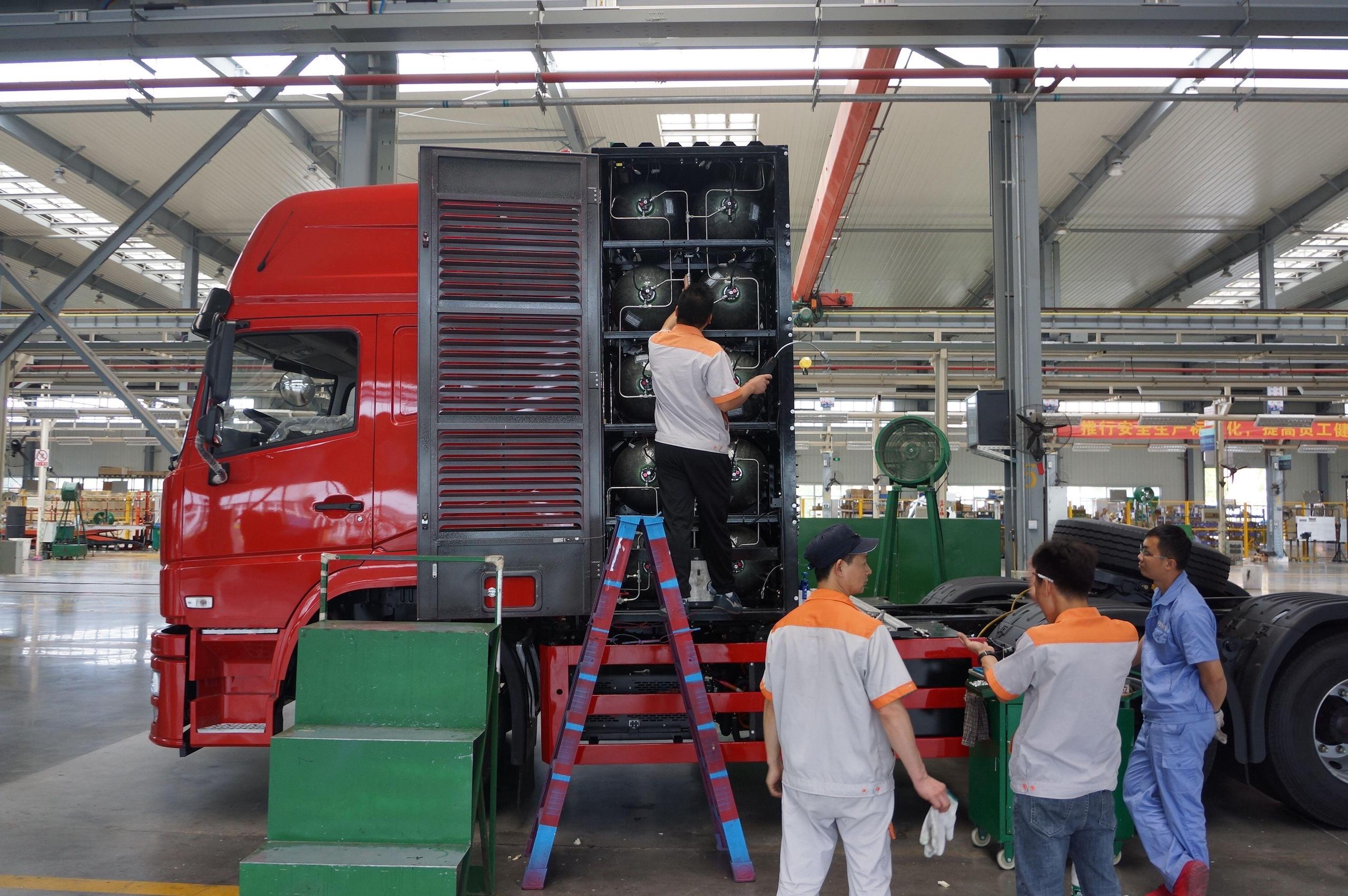 Workers standing next to a red lorry that is open on one side showing fuel tanks within