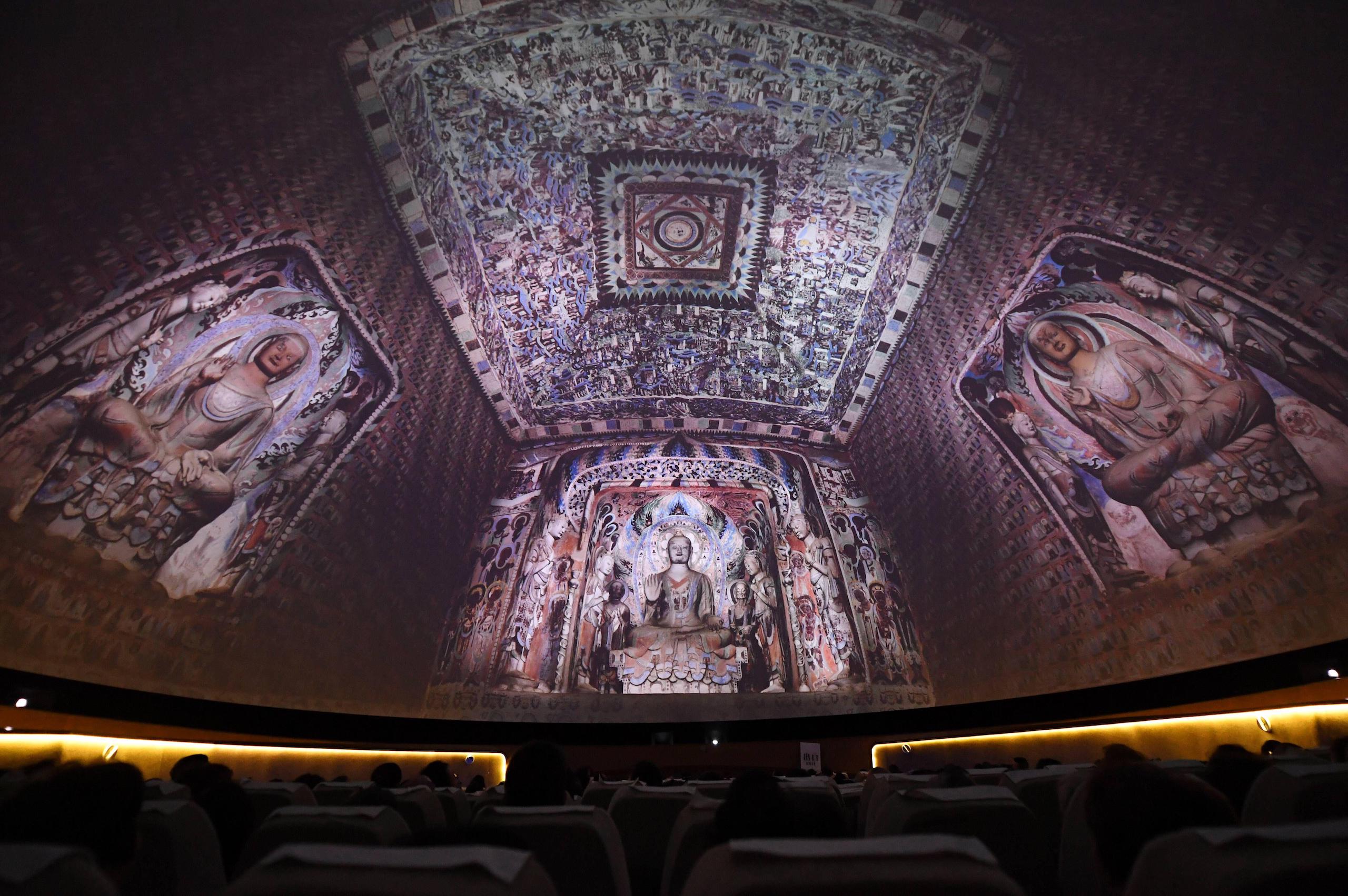 A dark auditorium with images of detailed cave drawings projected on the walls