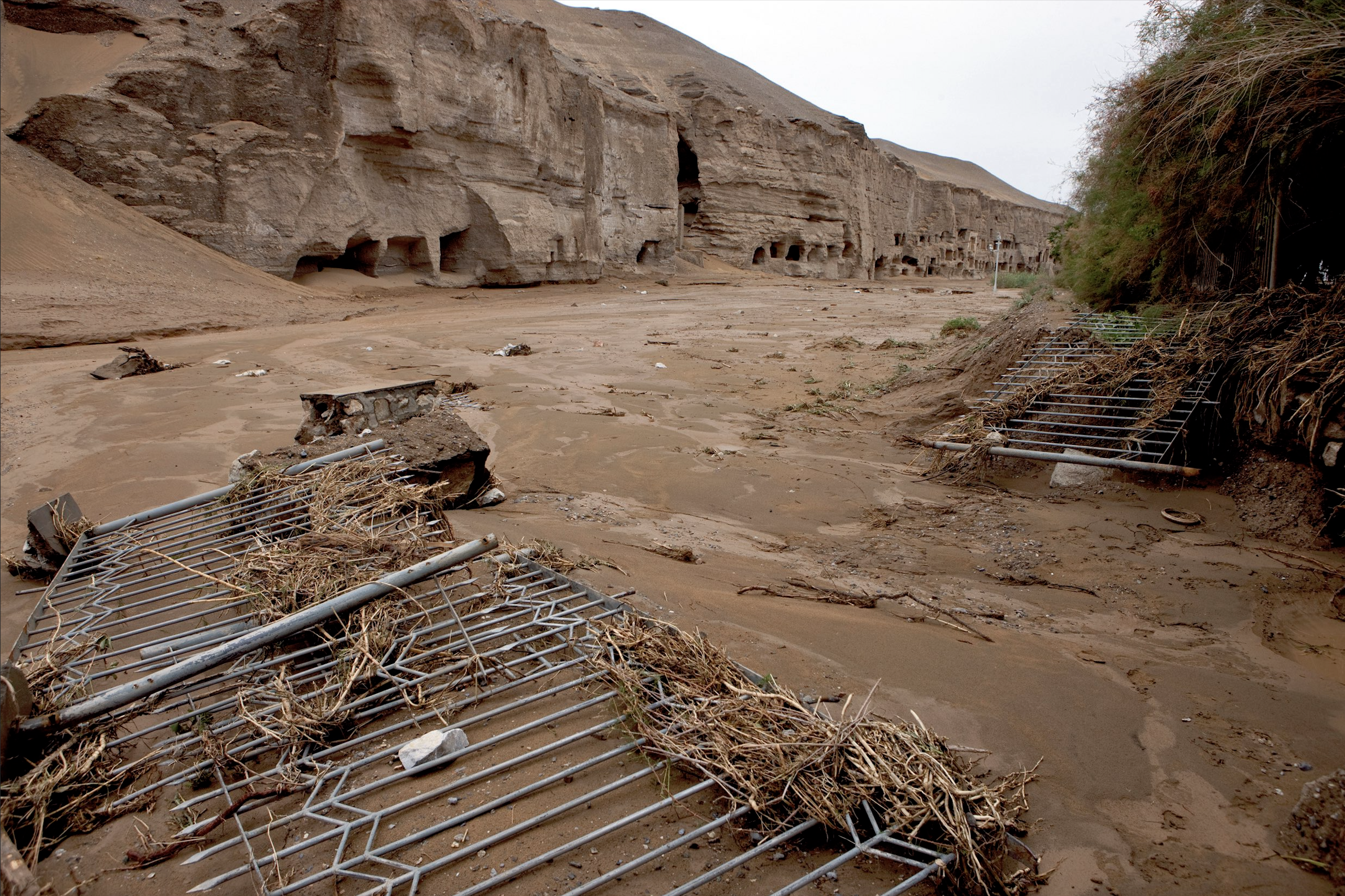 Overturned metal fences on a a sandy riverbank, caves in a cliff face in the background