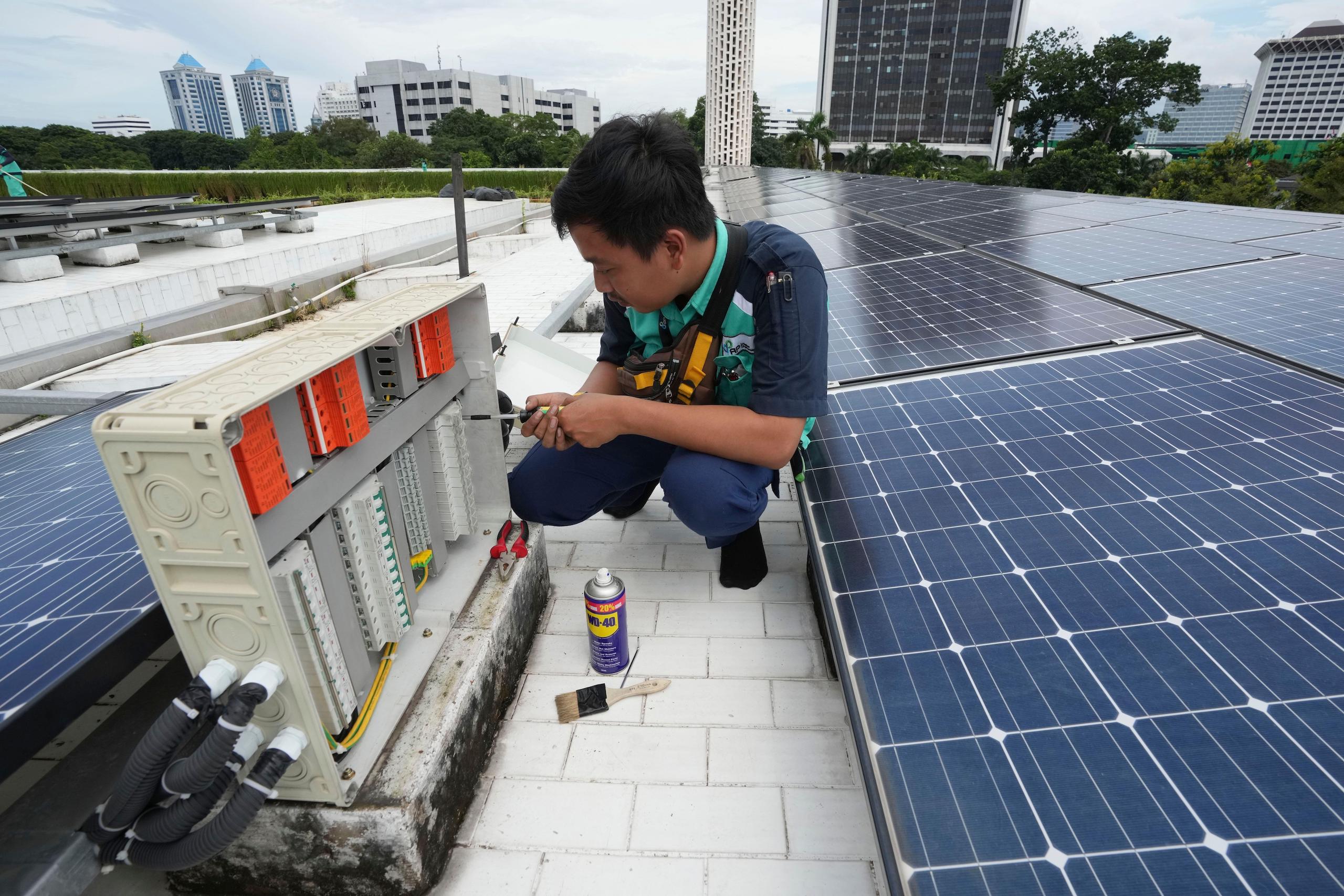 A man crouches next to an electrical panel, surrounded by solar panels