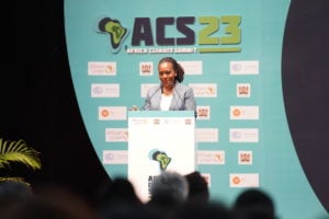 A woman speaks at a podium in front of a sign displaying 'Africa Climate Summit 2023'