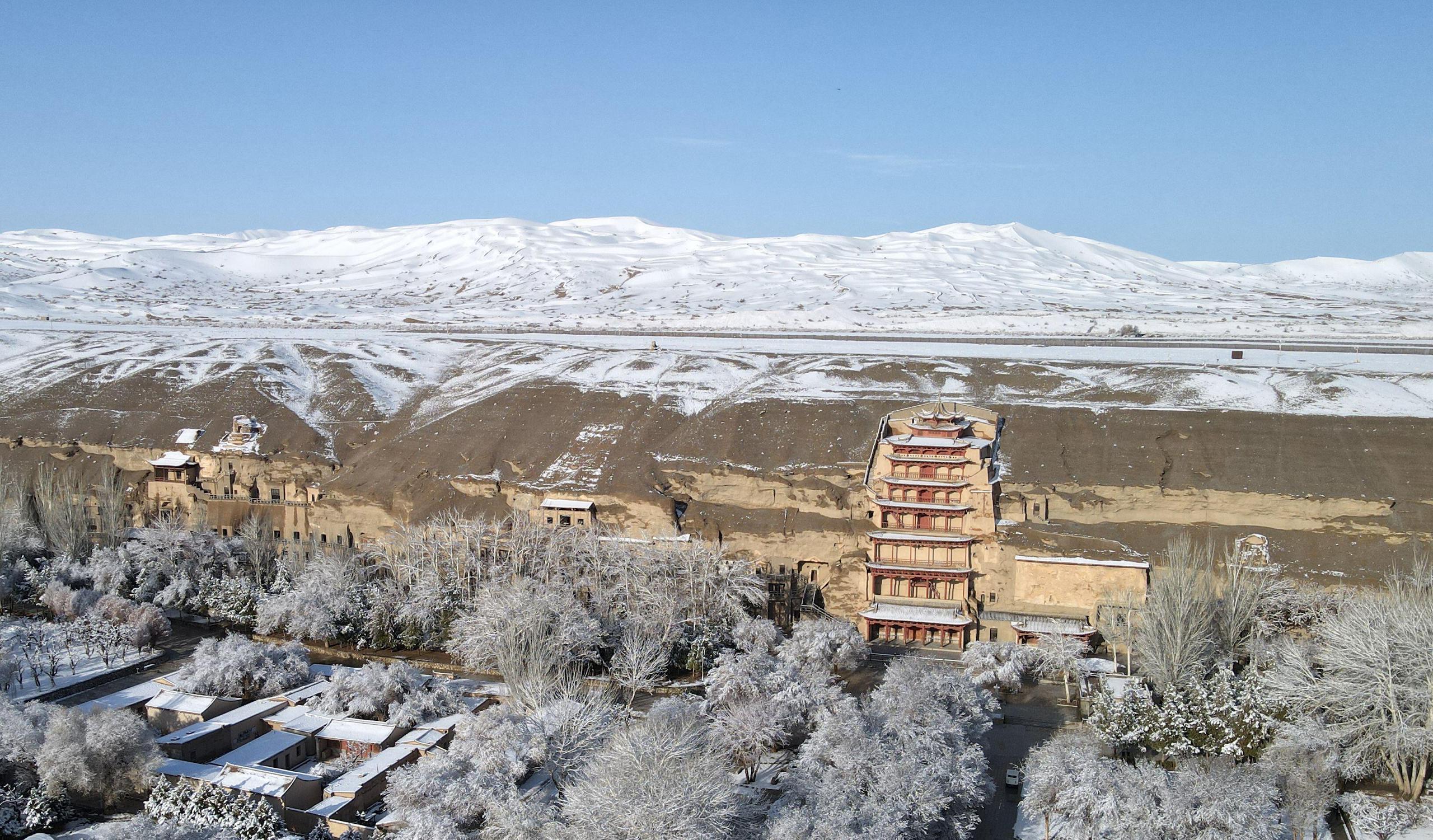 Aerial photo of a snowy scene, buddhist pagoda built into a cliff face, snow-capped moutains in the distance