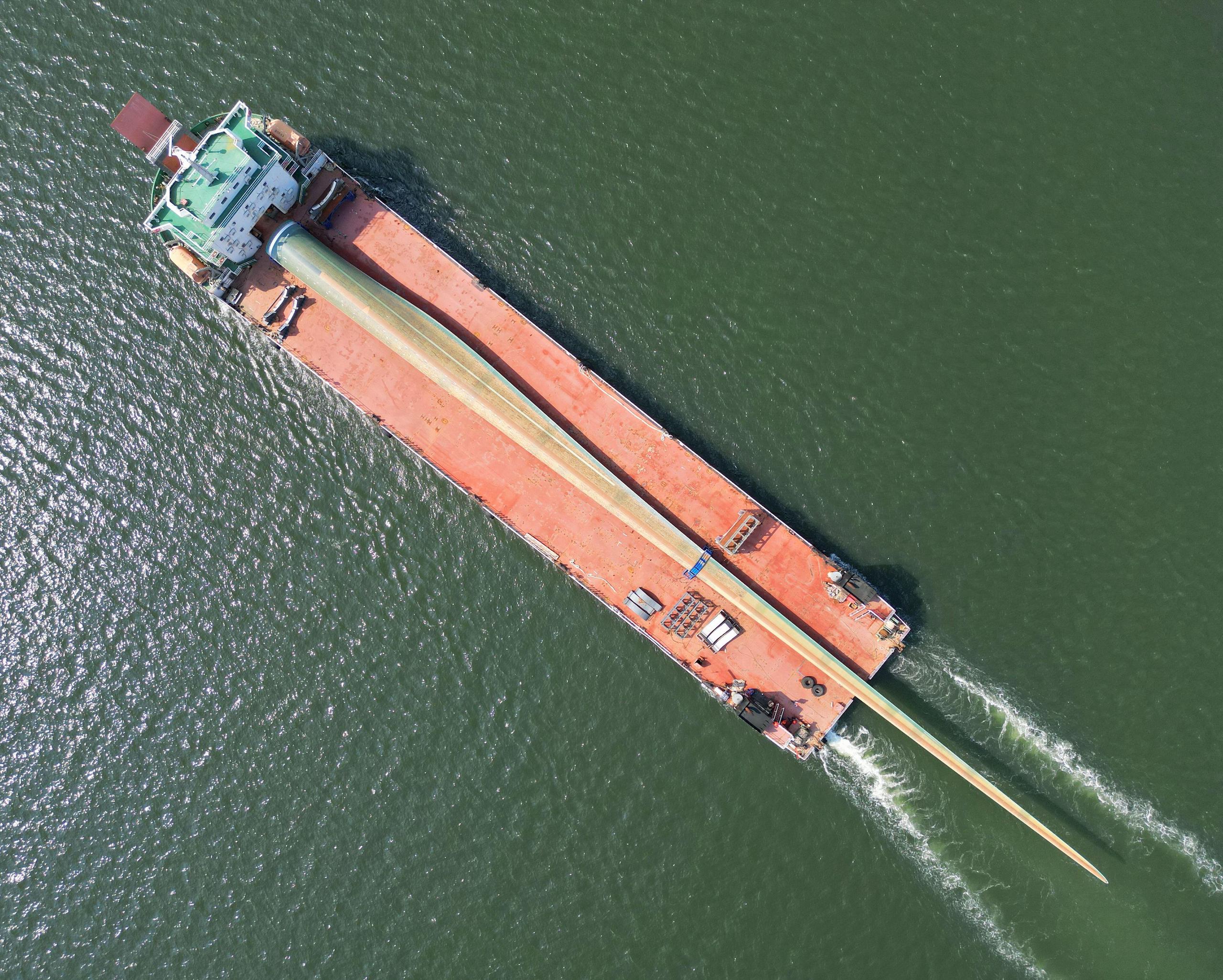 Aerial view of a cargo ship at sea carrying a giant wind turbine blade