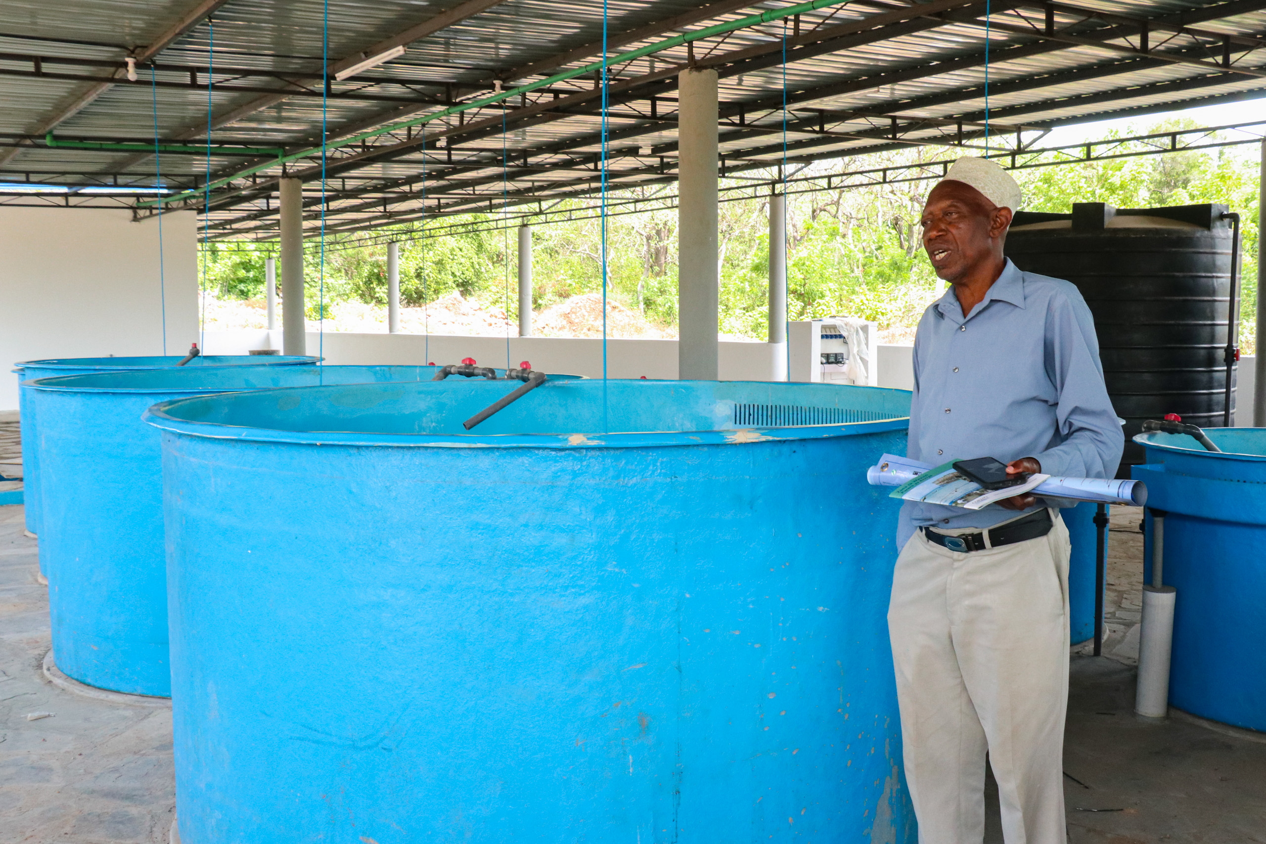Man speaking while standing next to waist-height blue tank