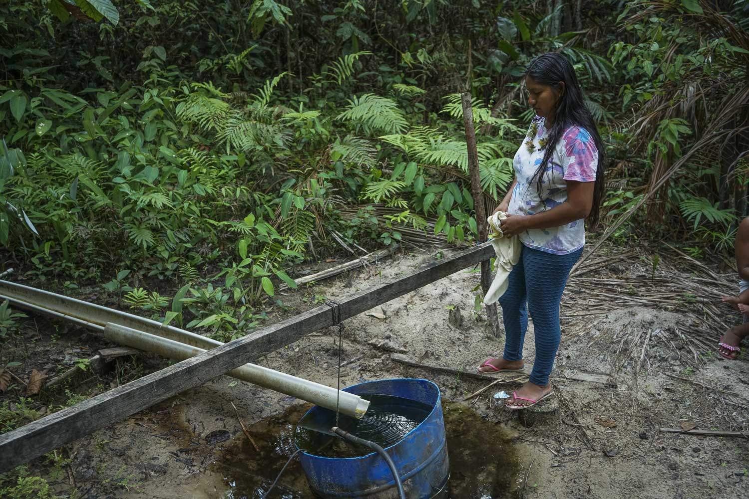 una mujer frente a vegetación y un pozo de agua