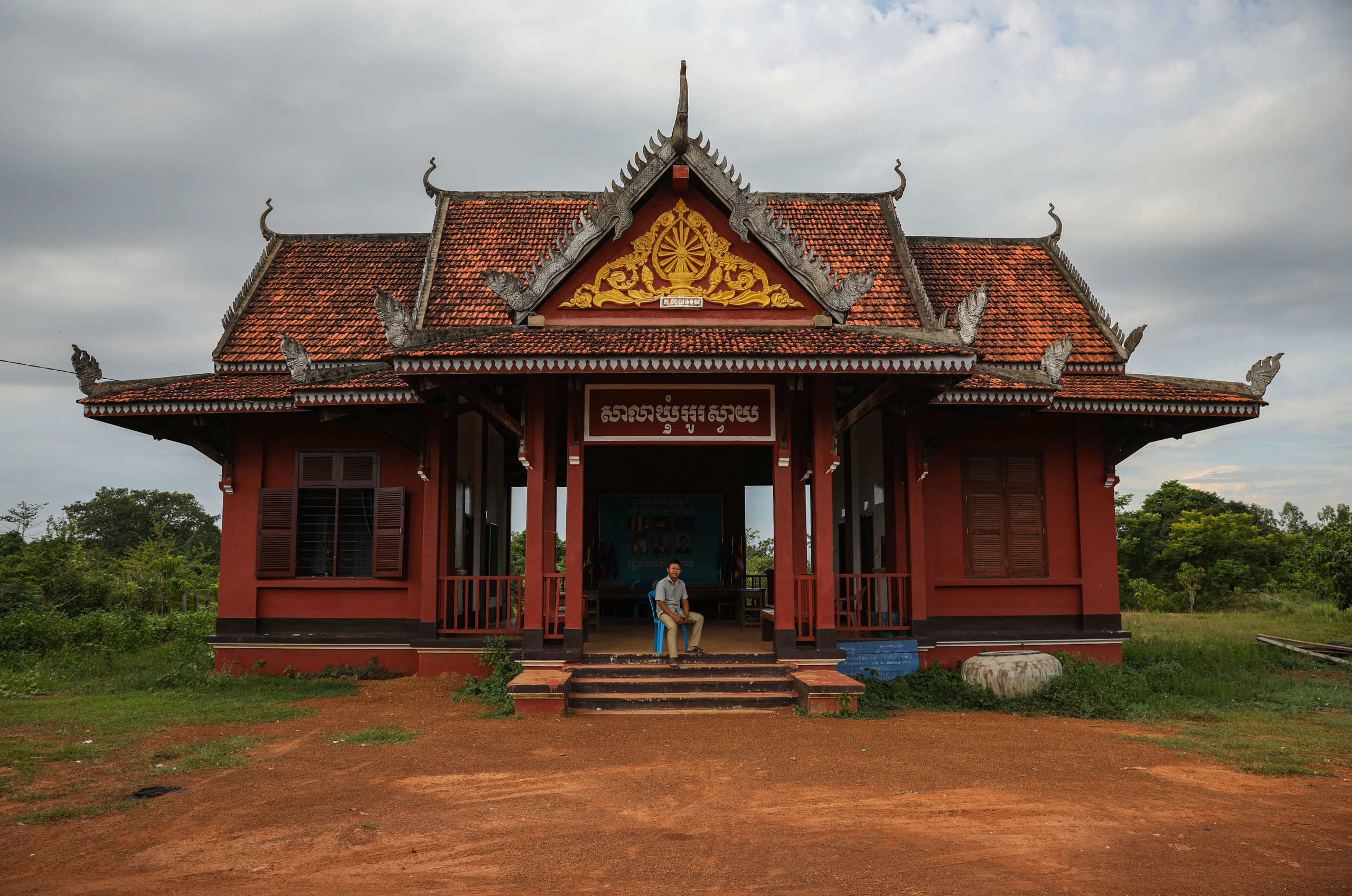 Red building with ornate tile roof, sign above entry way in Khmer