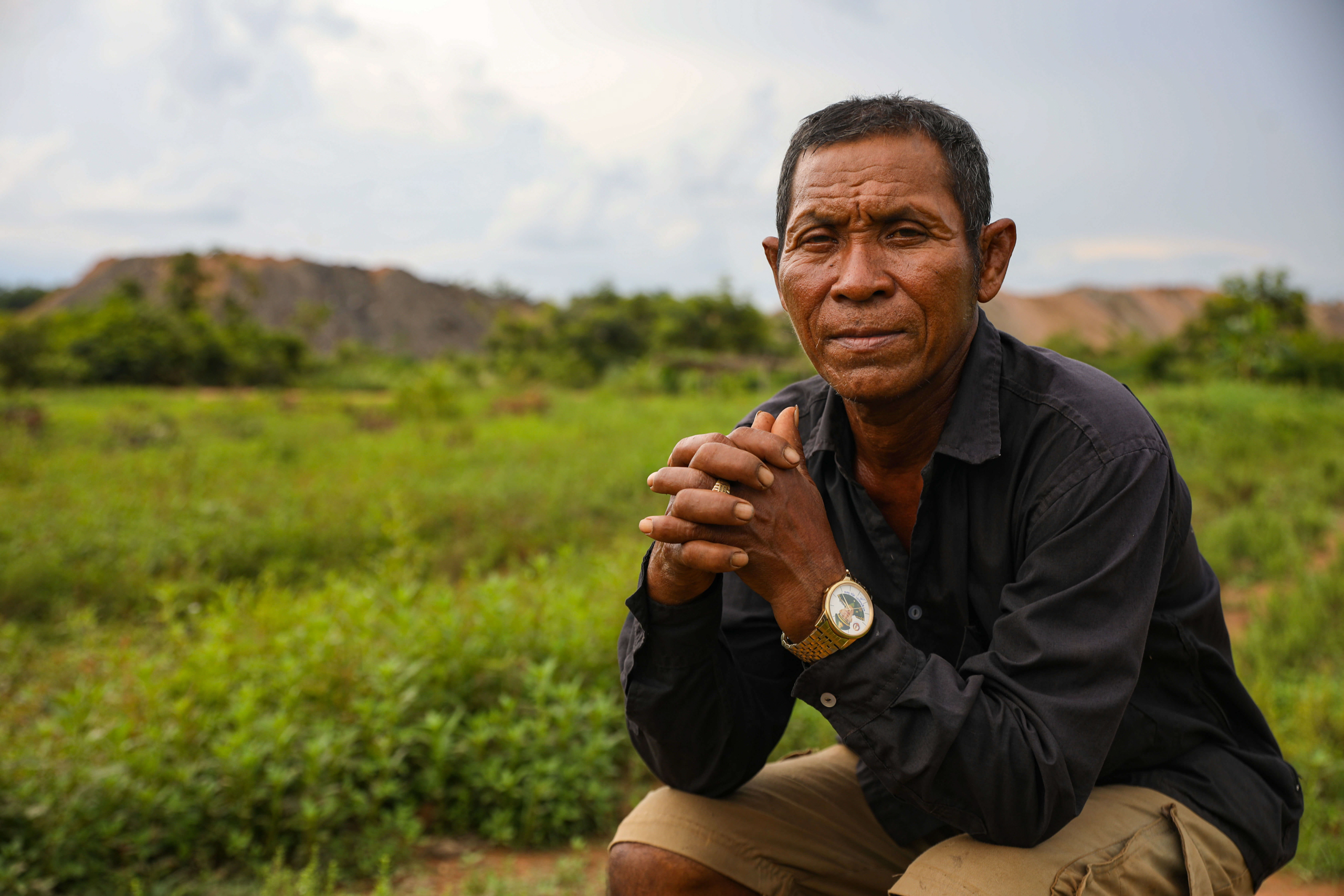 Man, sitting, with hands clasped looks at the camera