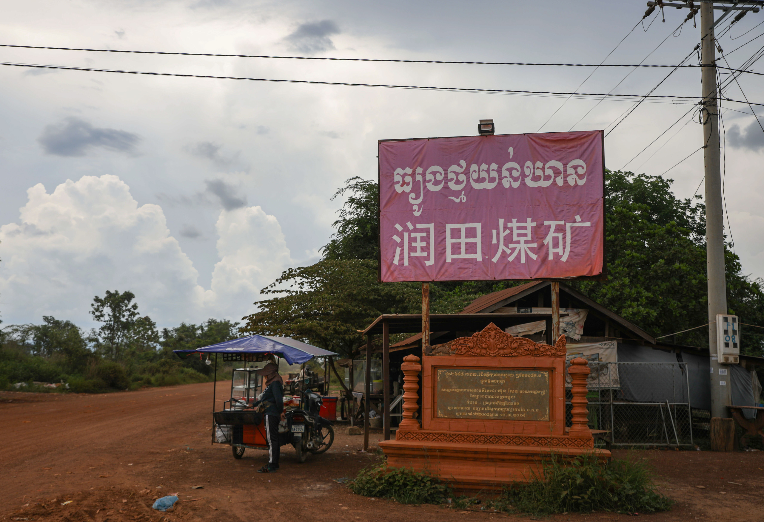 Faded red sign next to a road with Chinese and Khmer script on