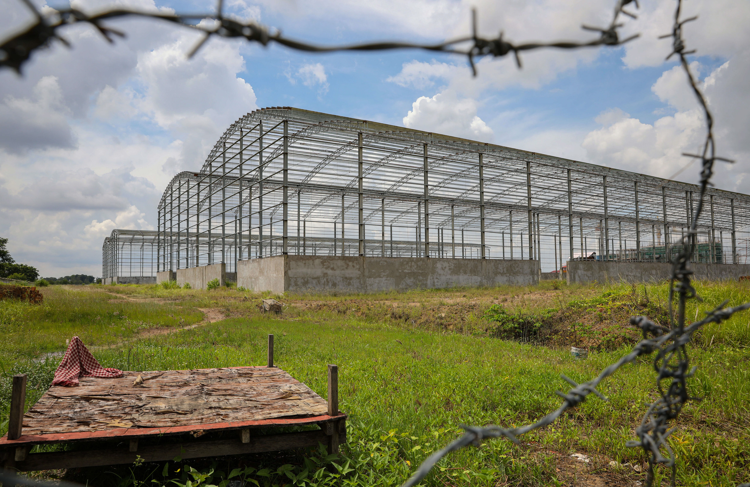 Skeleton of a building viewed through a gap in barbed wire fence