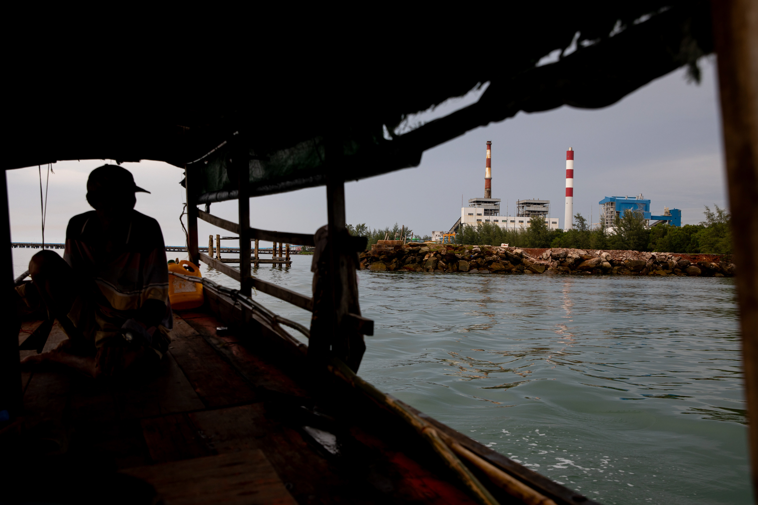 Smokestacks are seen from a boat next to the silhouette of a person