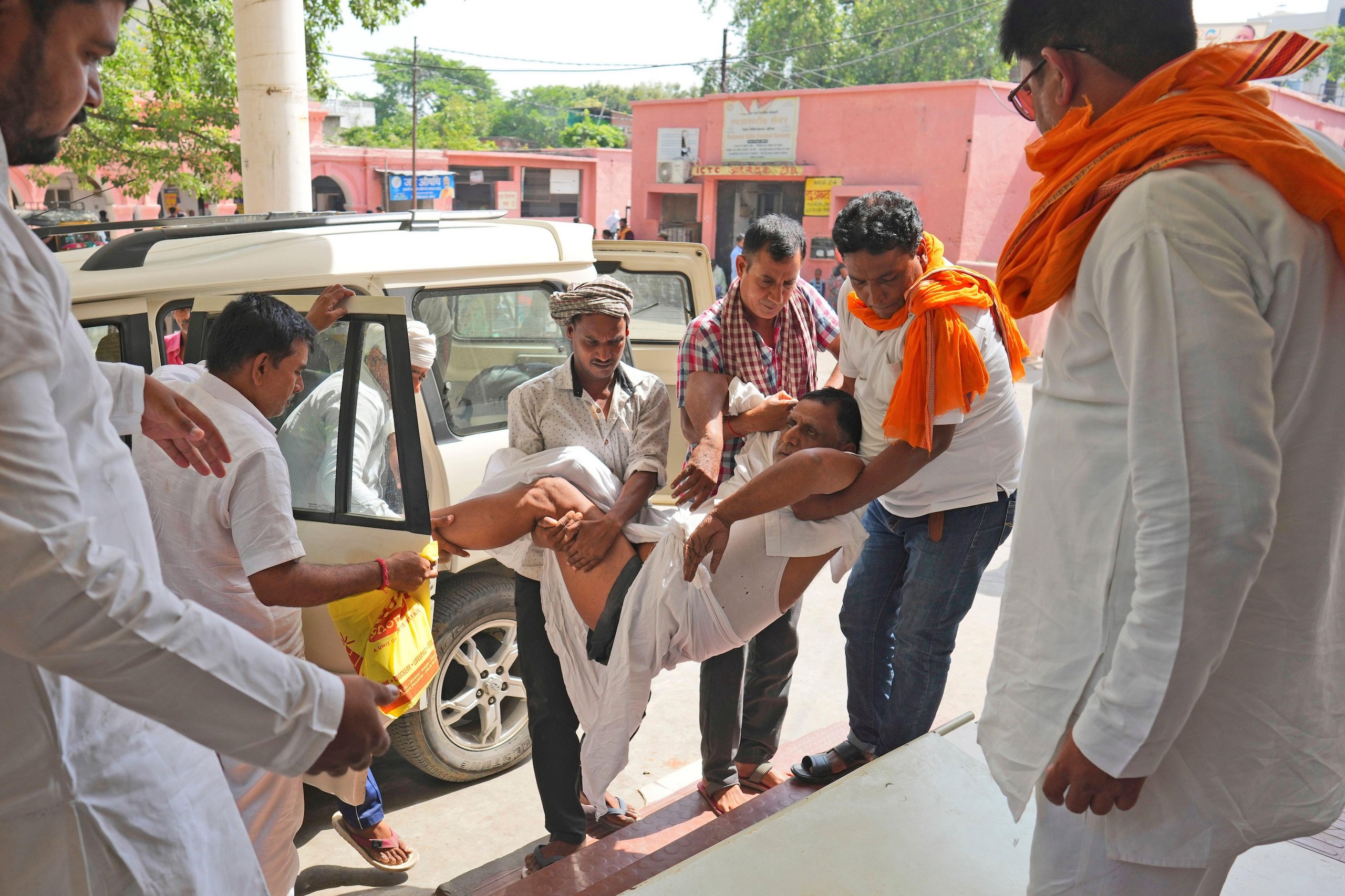 A group of people carrying an elderly man out of a car up some steps