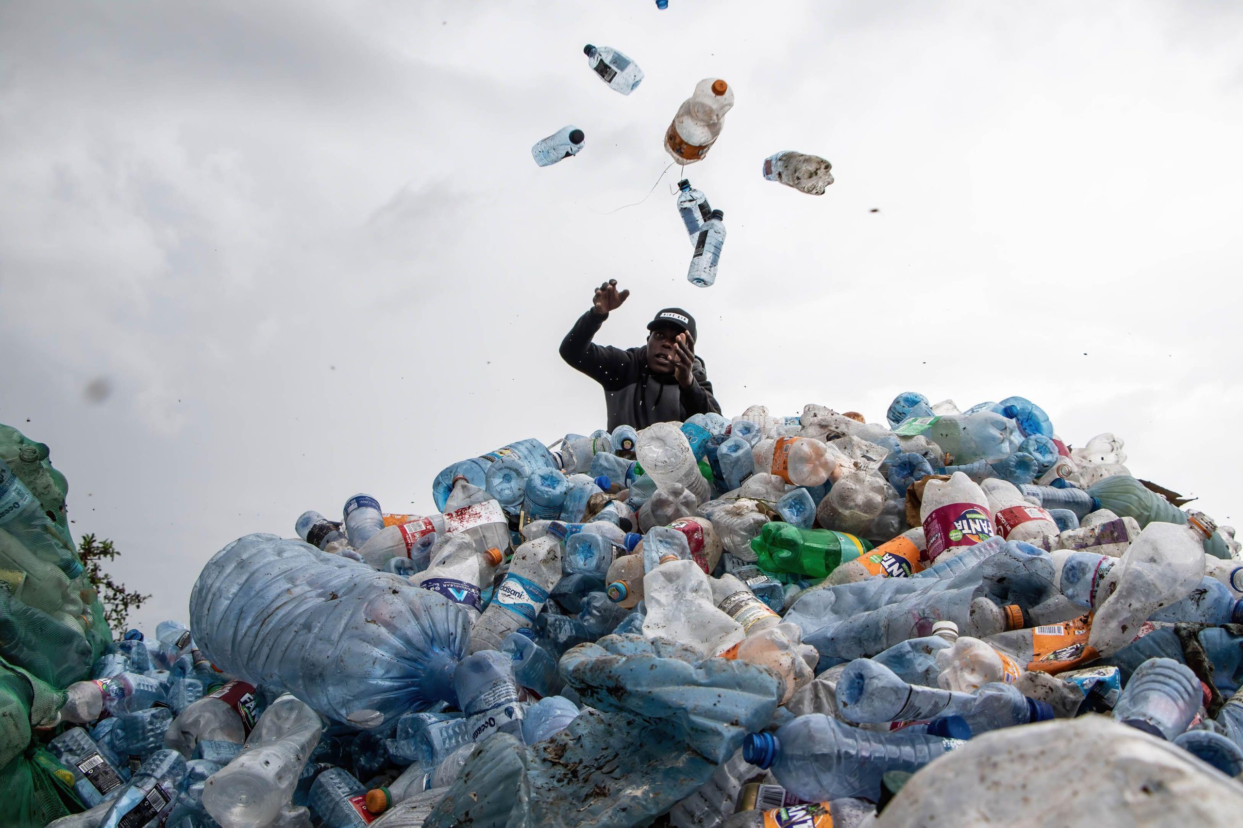 man piling plastic bottles onto heap of plastic waste