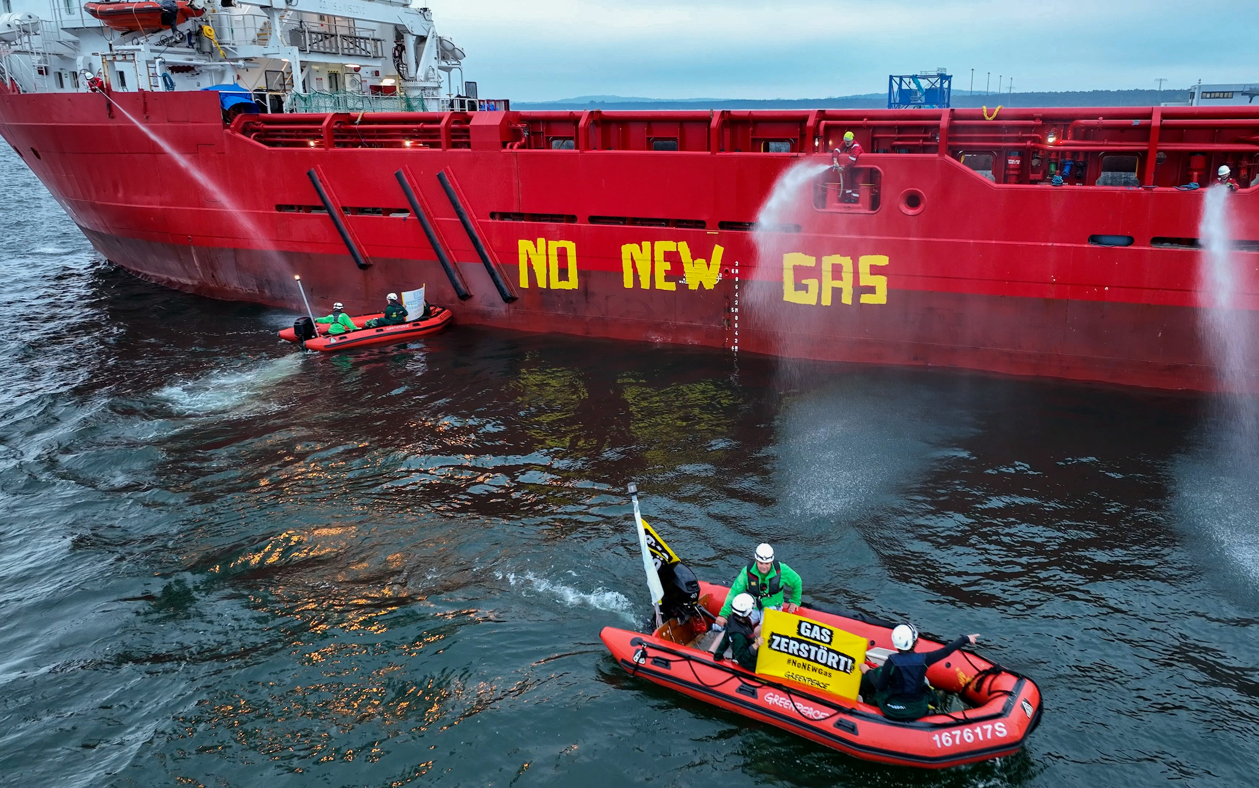 Small dinghies next to a large red ship painted with the words 'no new gas' in English,
