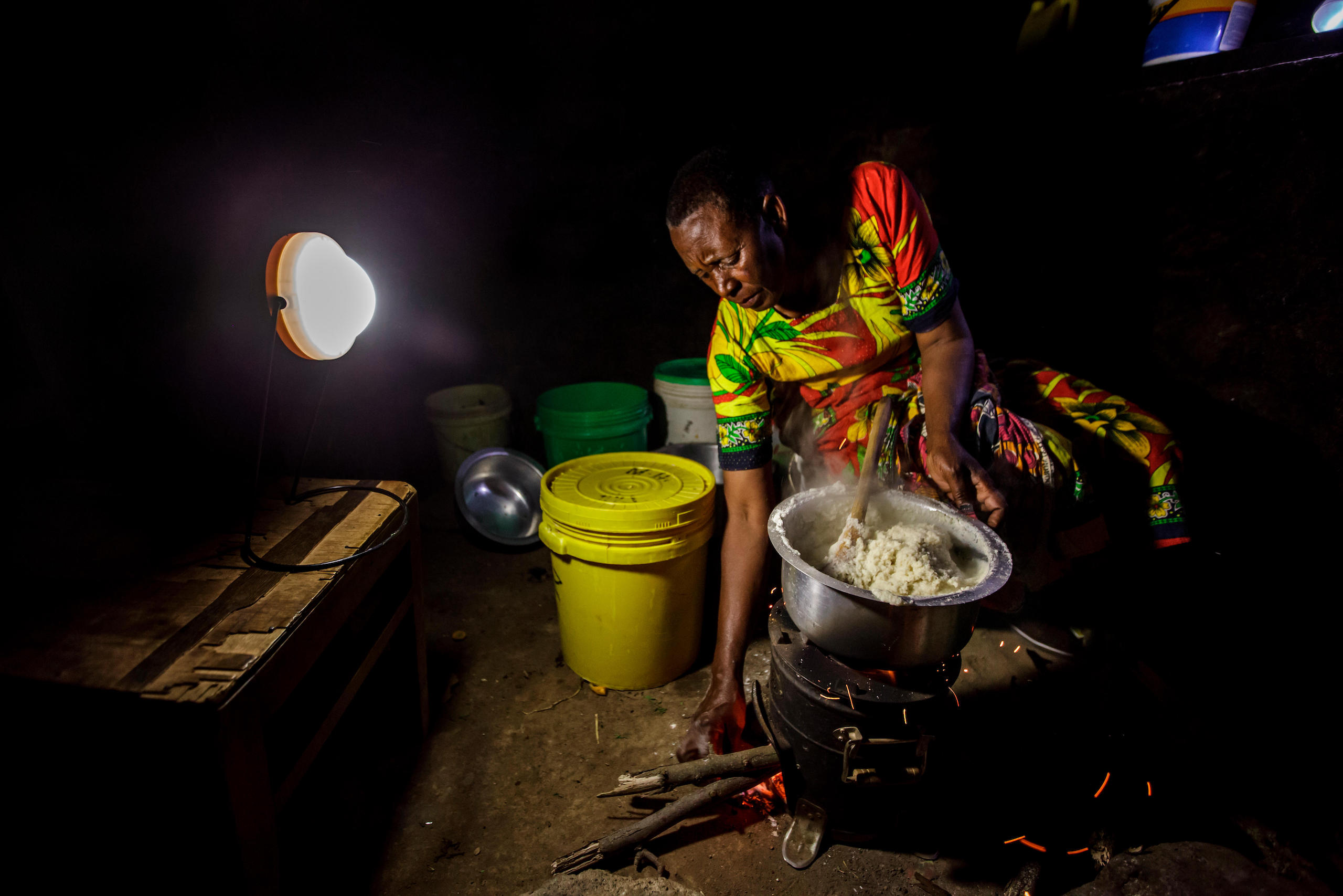 Woman cooking over a wood stove in lamp light