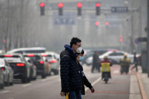 Two people wearing face masks cross a busy street in hazy conditions