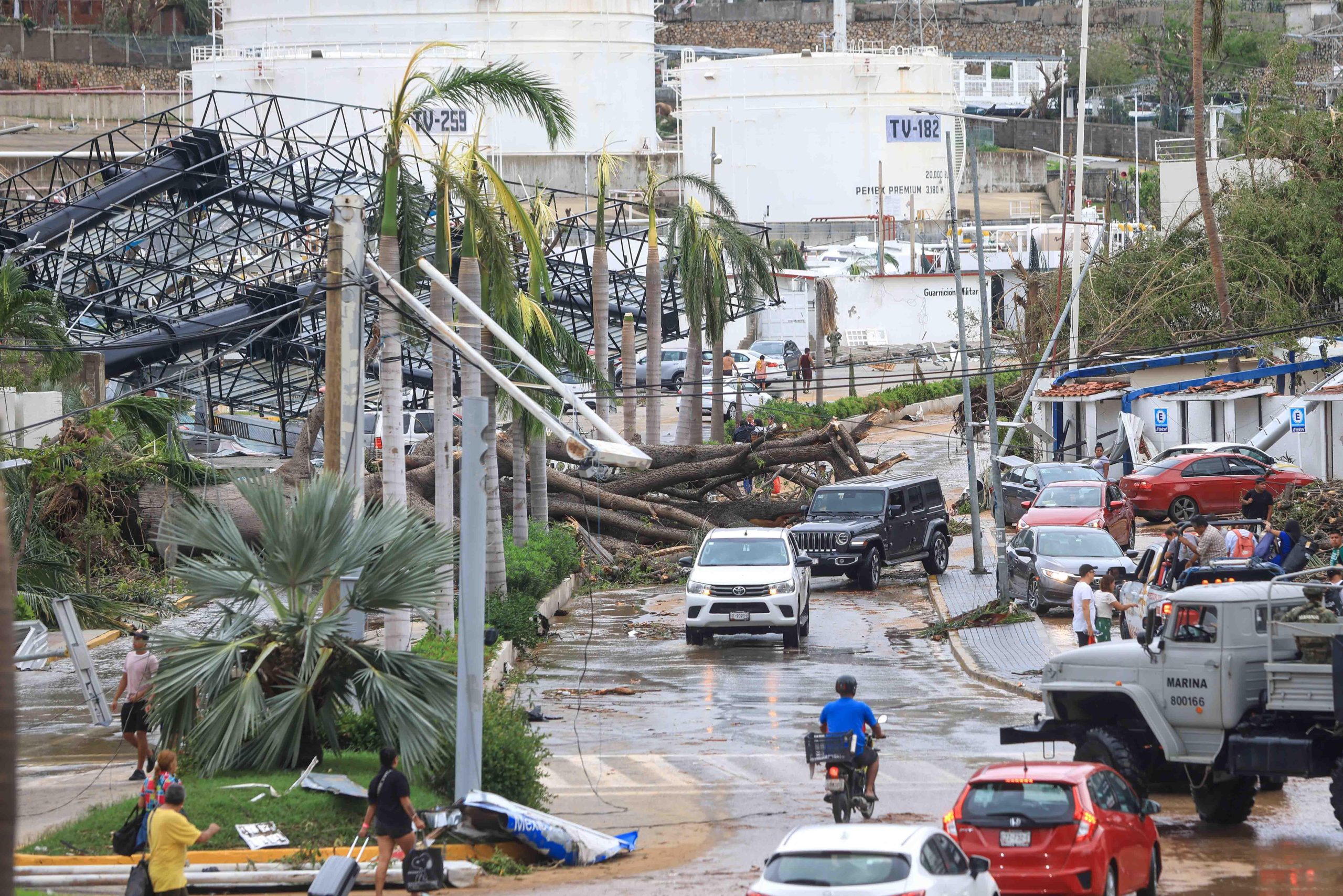 vehicles on wet street with fallen branches and infrastructure