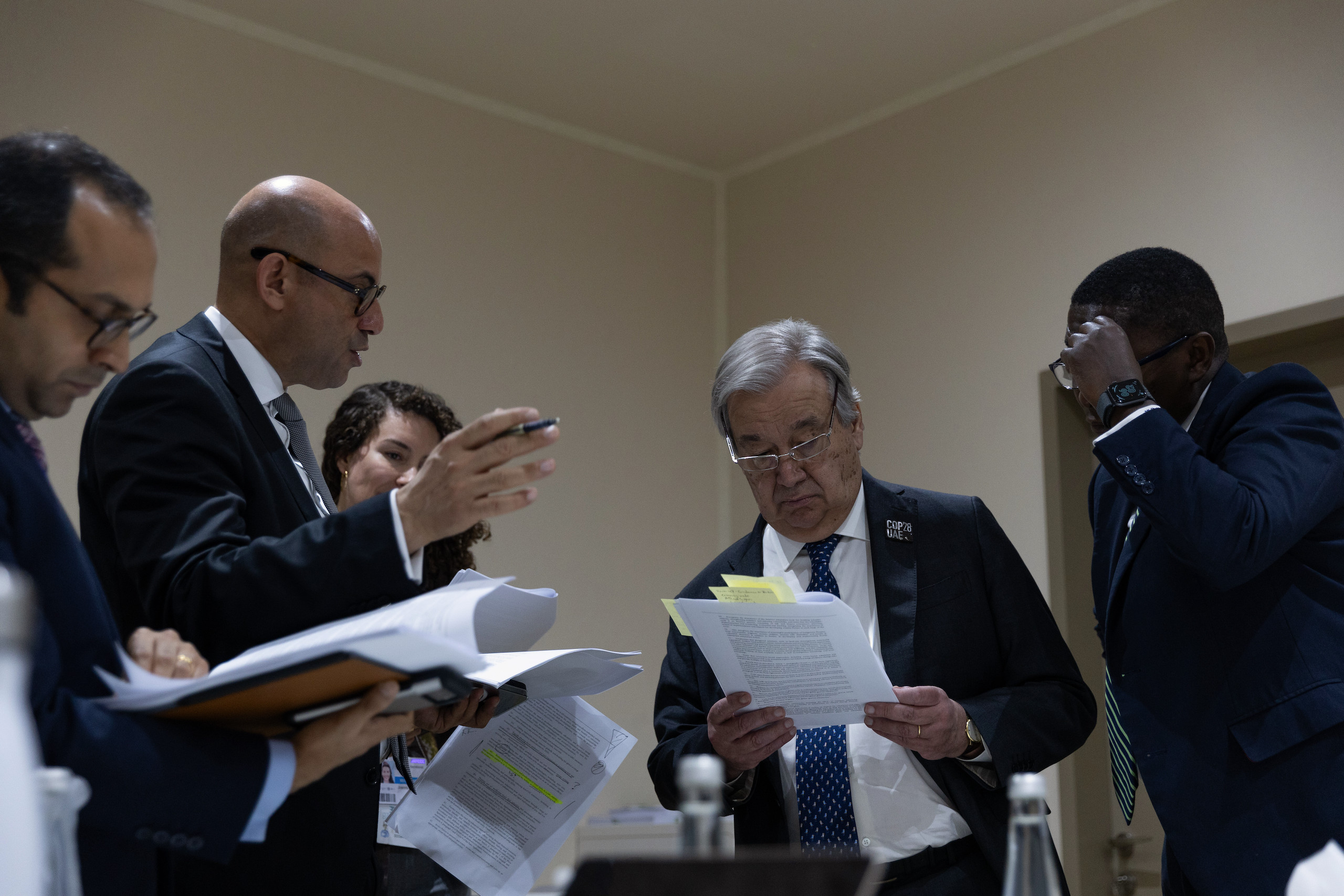 Suited men standing in a small room reading documents