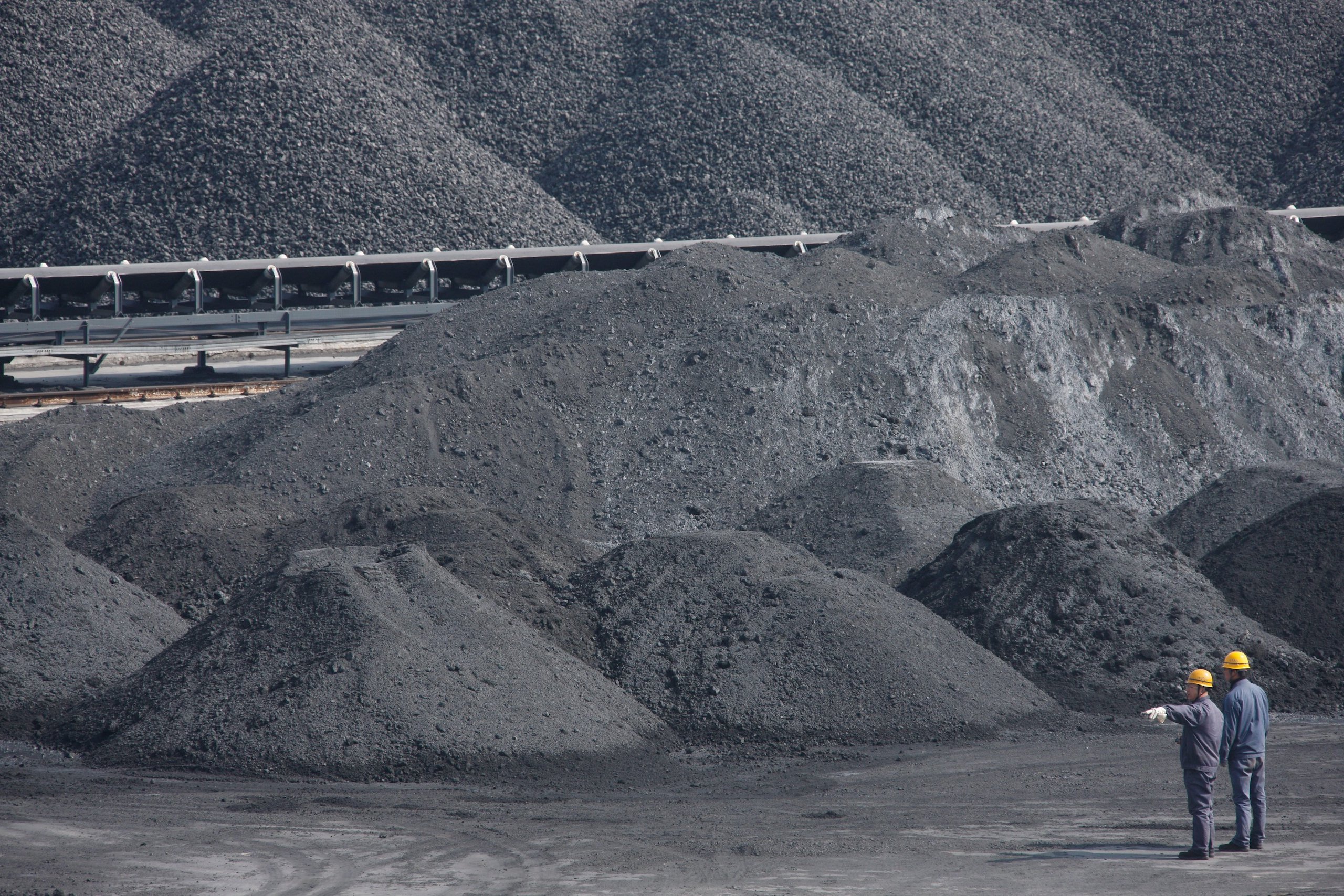 Two workers stand in front of heaps of black coal dust
