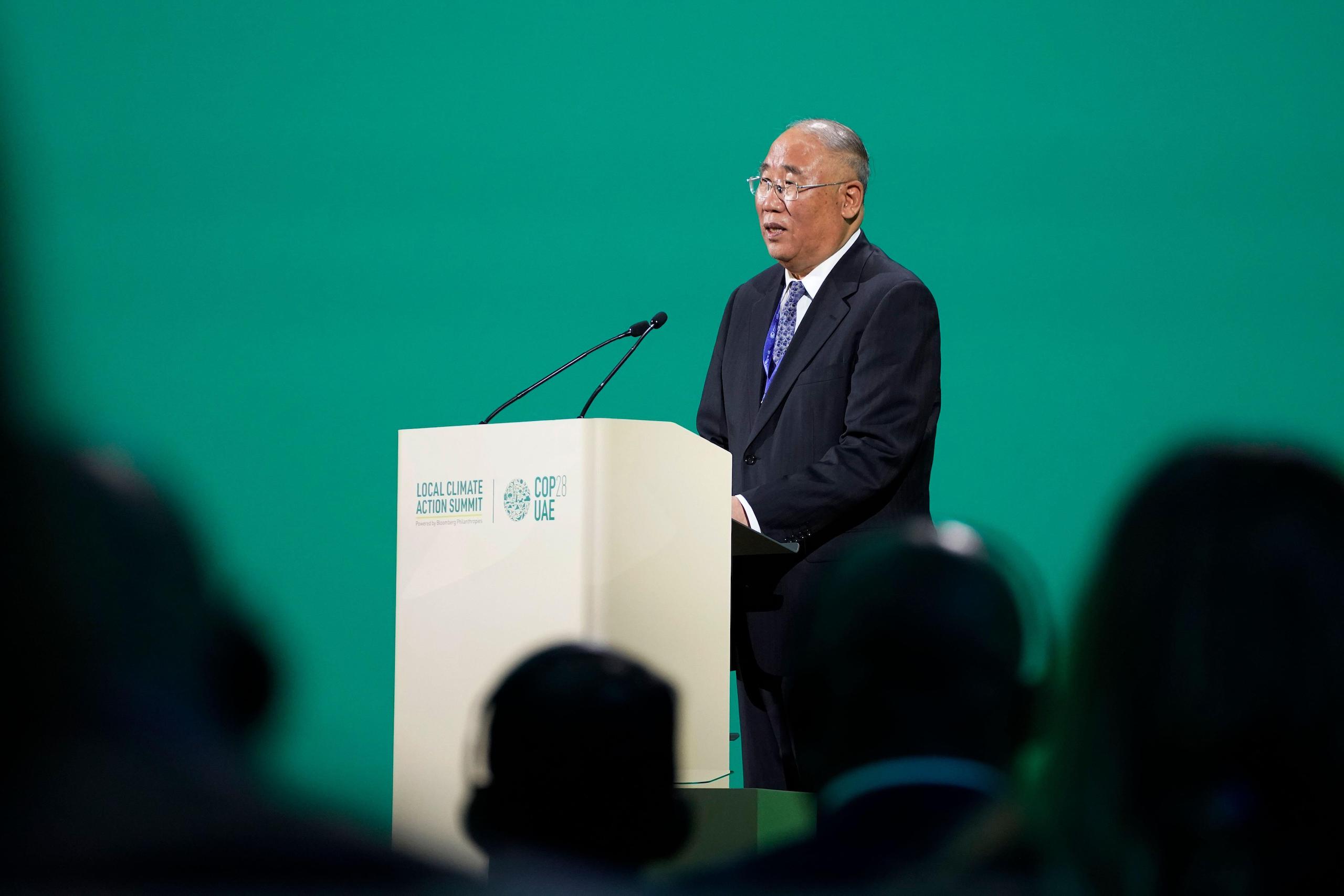 Suited Xie Zhenhua stands at a podium speaking into a microphone, green background