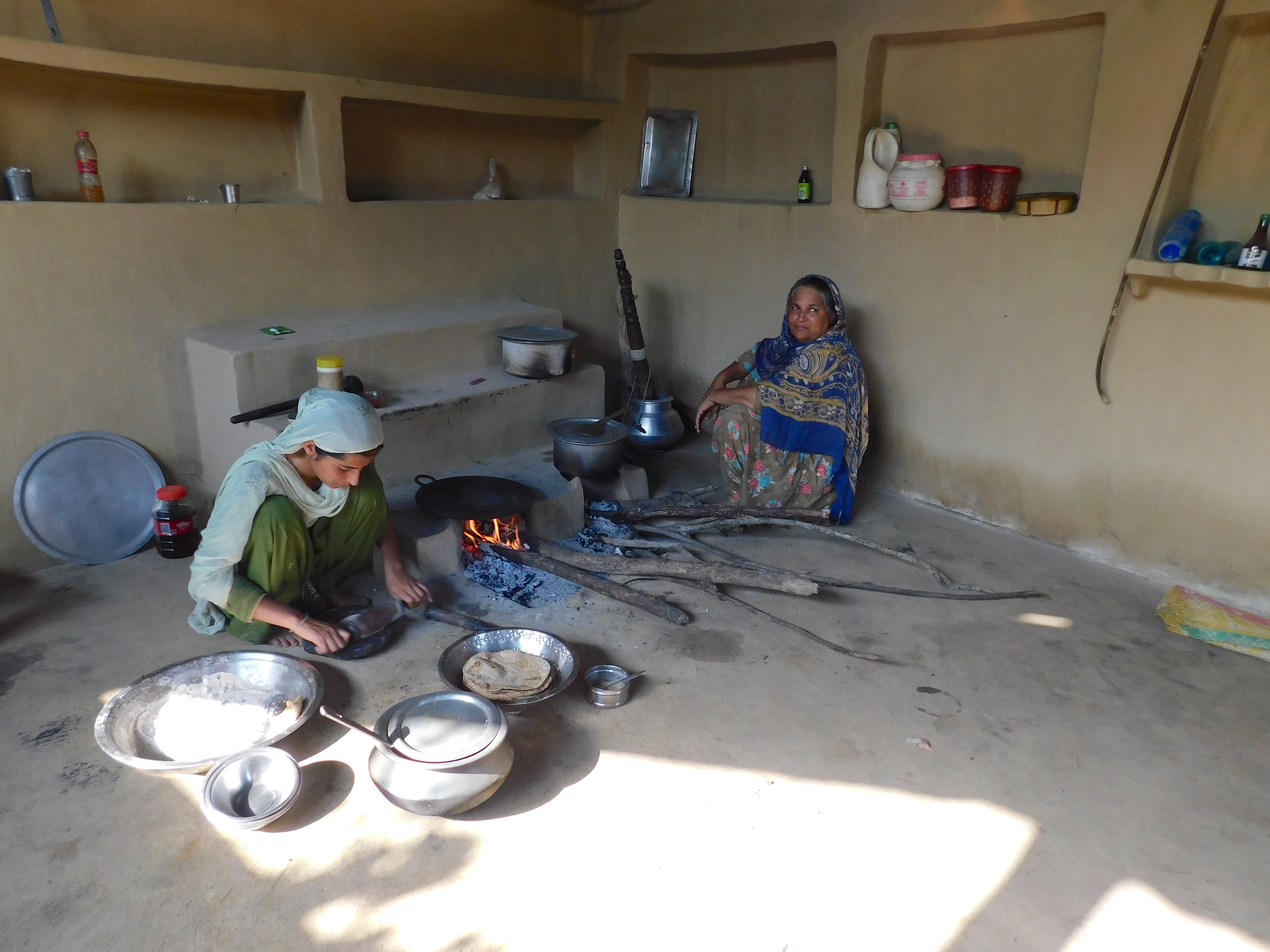 two women cooking on woodfired stoves in a room