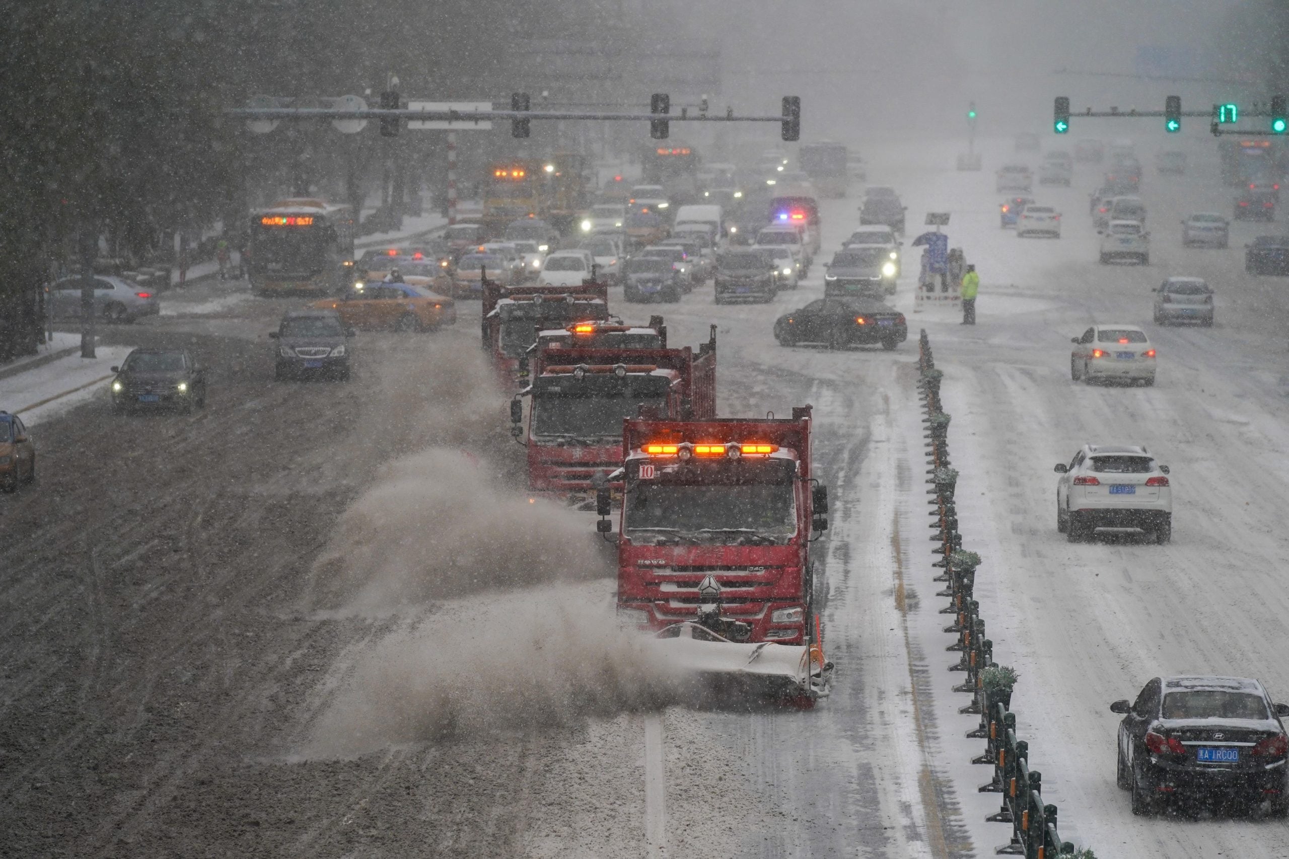 Snow plow trucks clear snowy road with heavy traffic