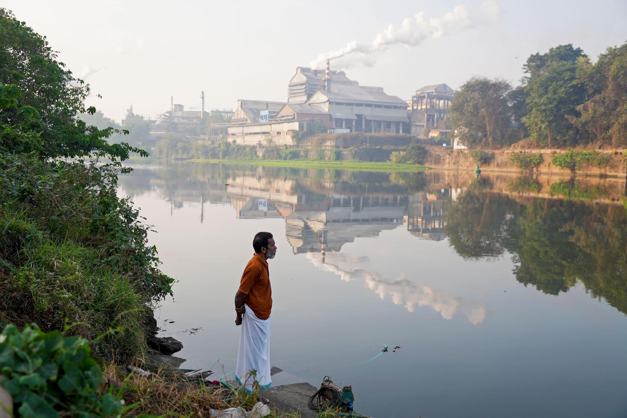 Person standing next to a river, petrochemical factory in the background