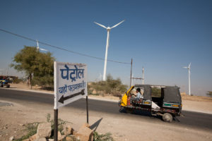 A three-wheeler vehicle drives past wind turbines in a desert