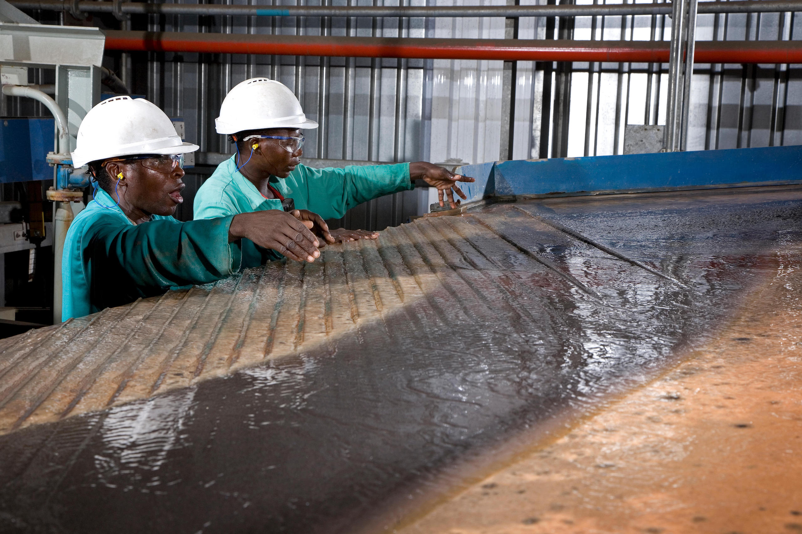Workers in hard hats gesture at a pool of water on a table