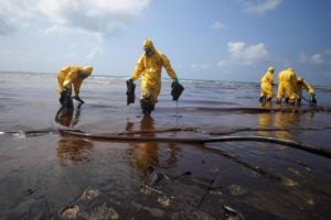 People in yellow hazmat suits clean up oil from a beach