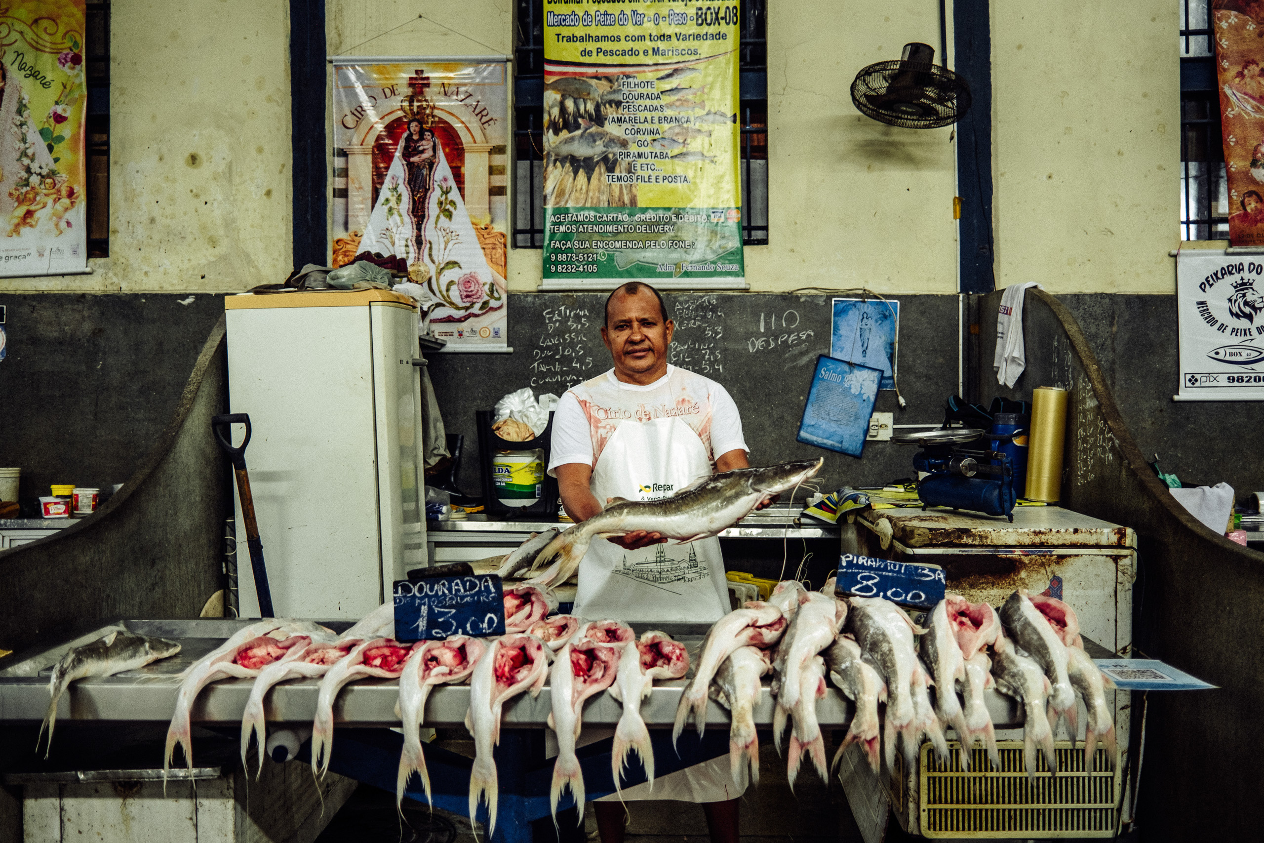 Un hombre sosteniendo pescado eviscerado detrás de un expositor con más pescado