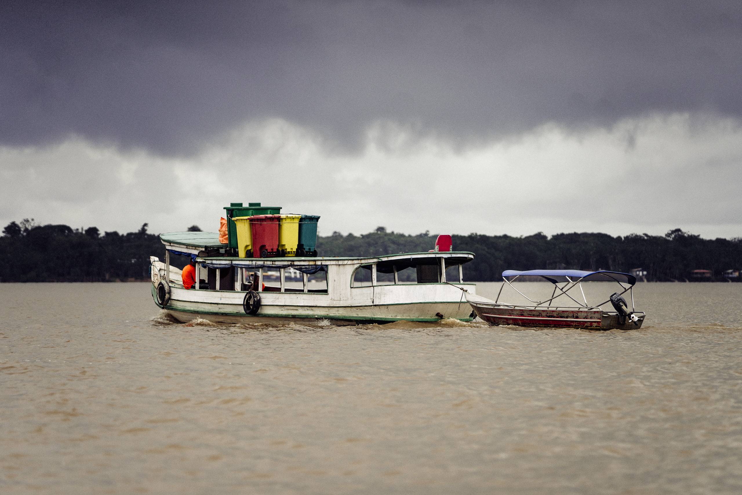 two boats on river, one filled with large garbage bins