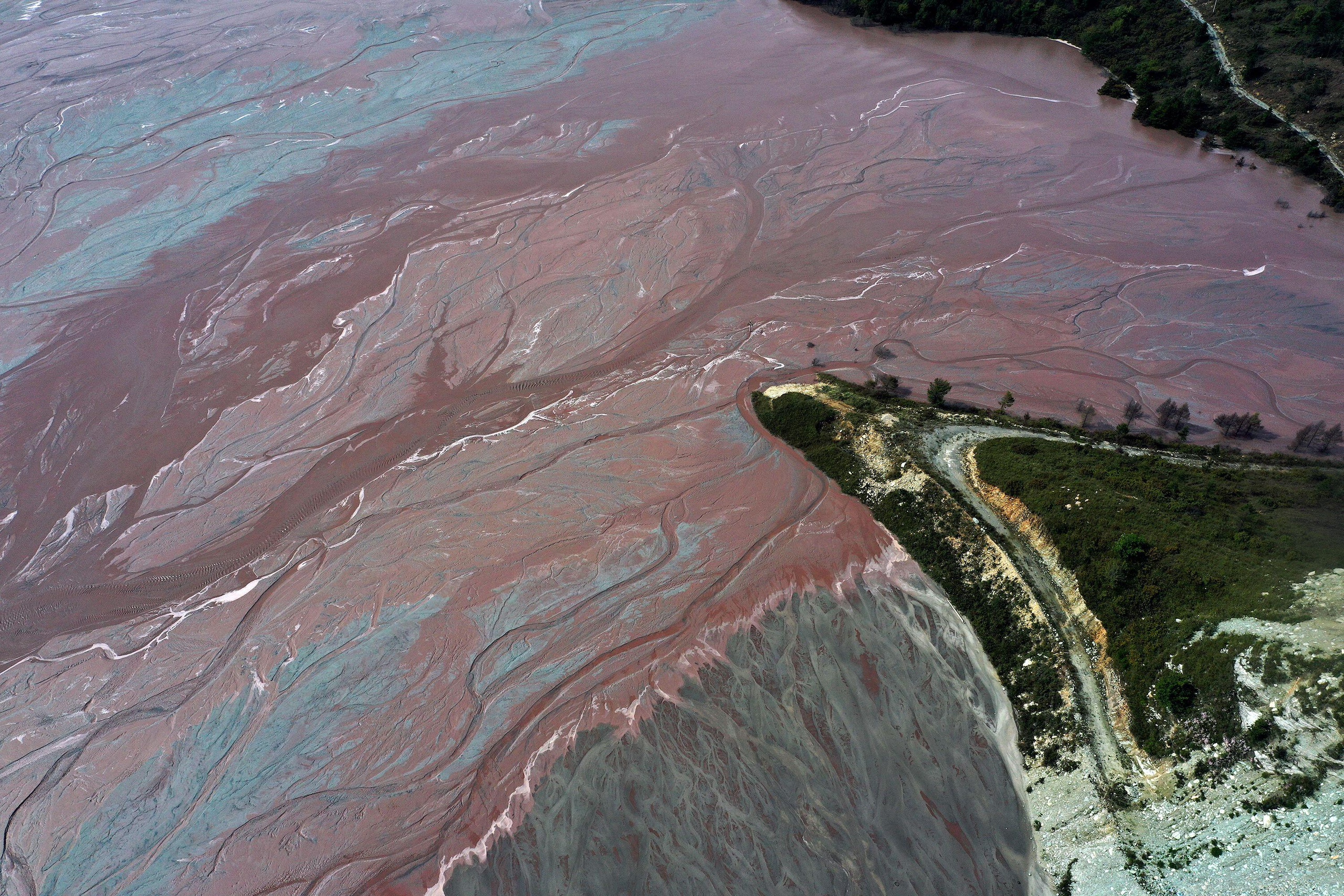 Aerial view of a lake covered with stripes of pink purple and blue sediment; pollution