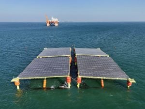 Four solar panels floating on the ocean, an offshore platform in the background