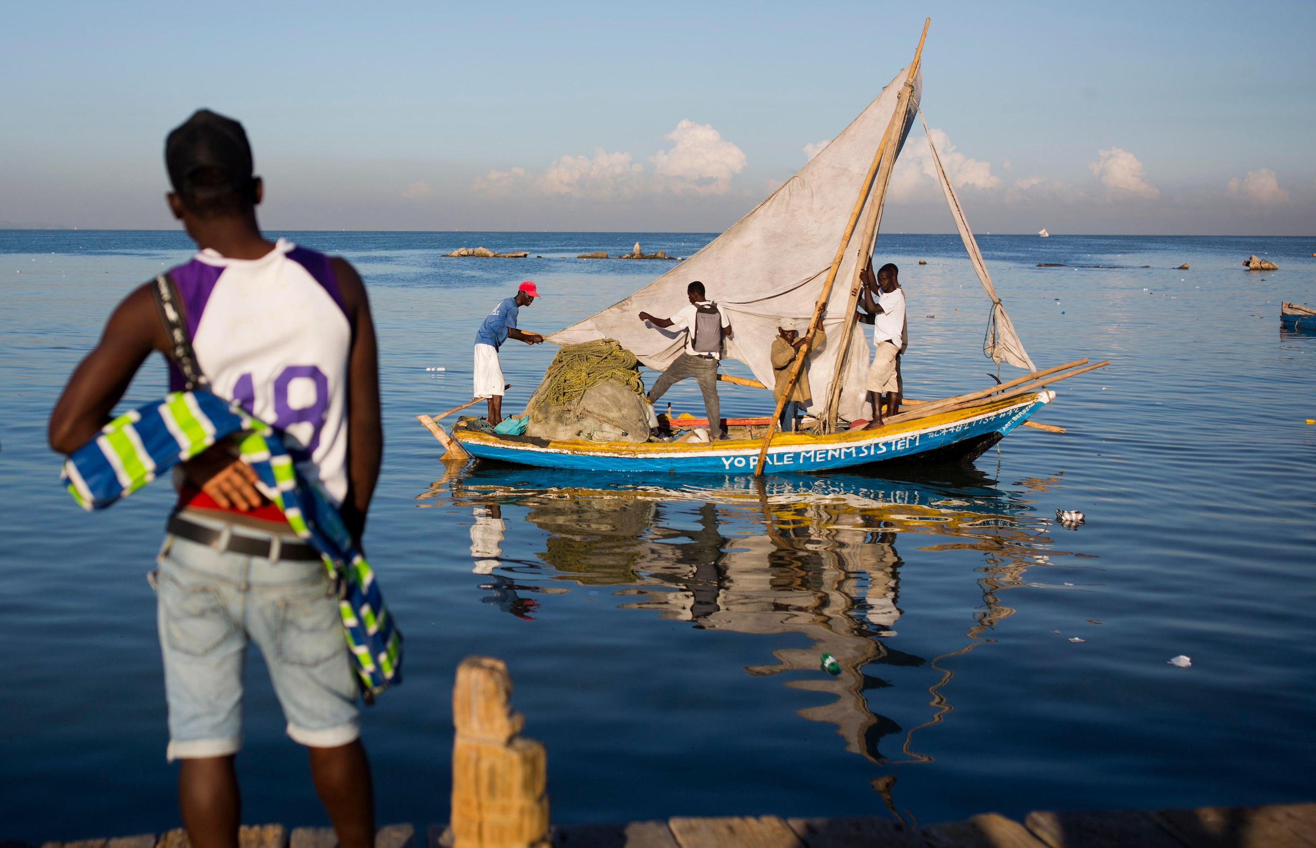 A man looks out at people fixing a small fishing boat on the water