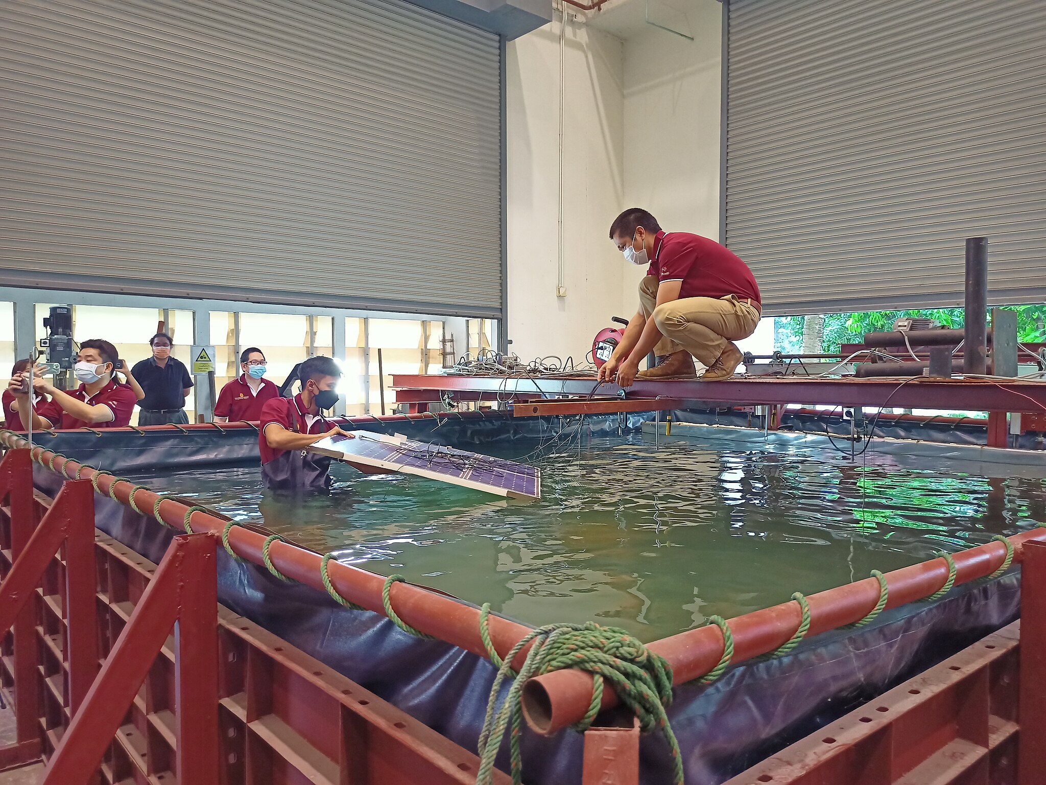Two researchers in a laboratory lay solar panels on the surface of water in a large tank
