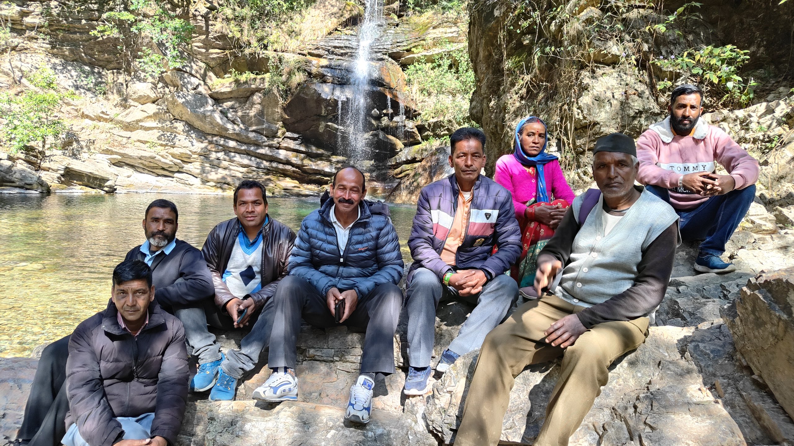 Group of adults sitting on rocks beside a small waterfall in a forested area