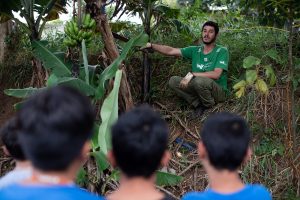 Un hombre con una remera verde enseñando a niños en una zona boscosa