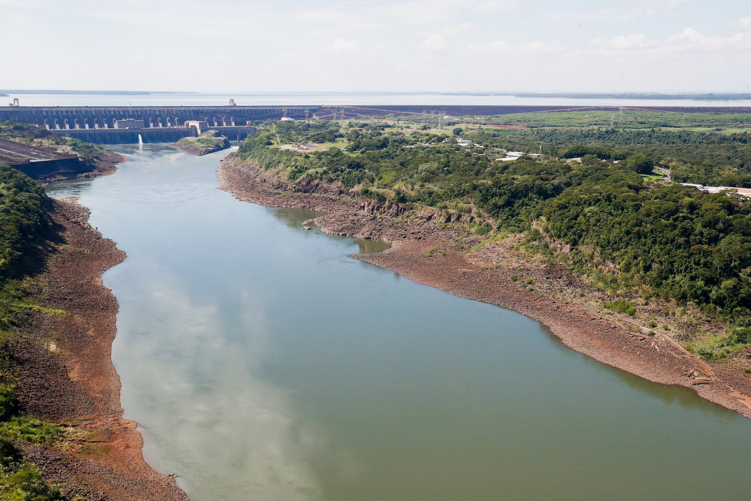 A large body of water surrounded by trees with a large dam in the background 

