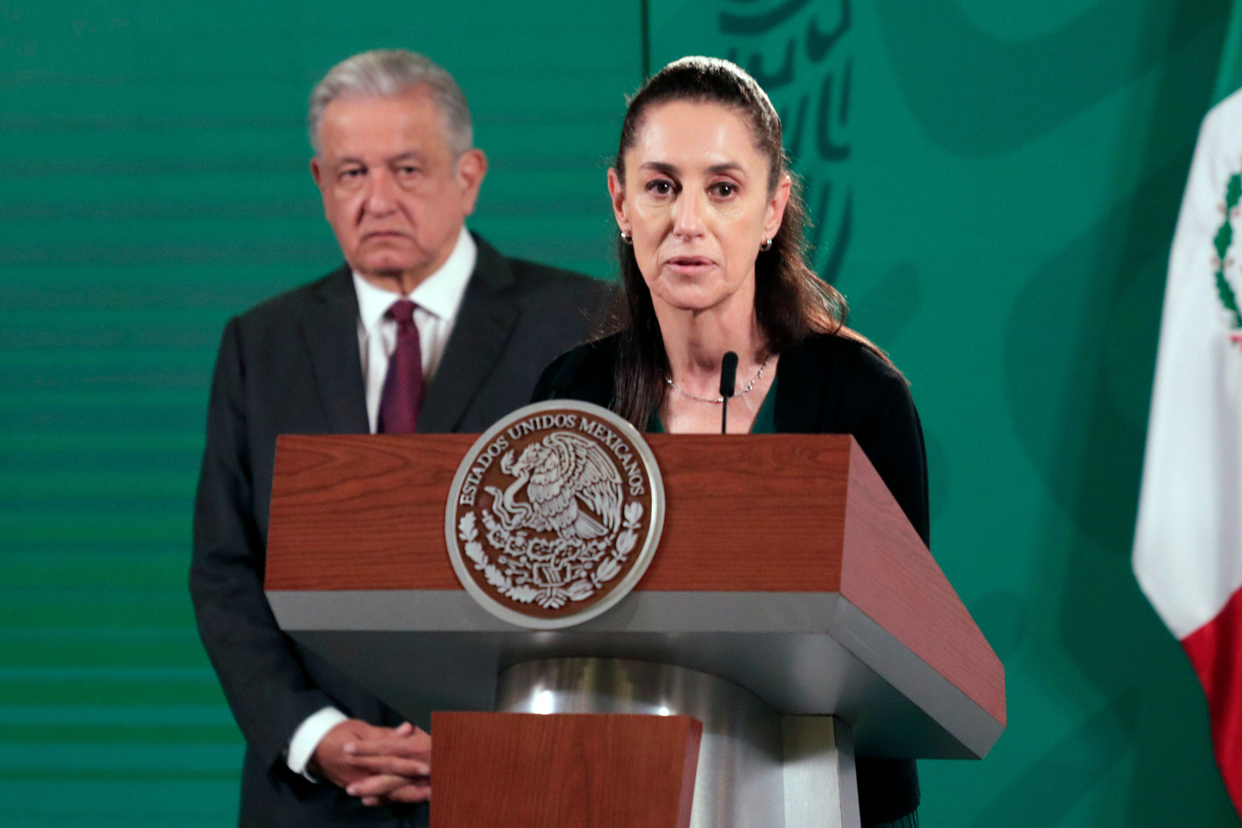 Claudia Sheinbaum hablando frente a un estrado, y AMLO detrás suyo