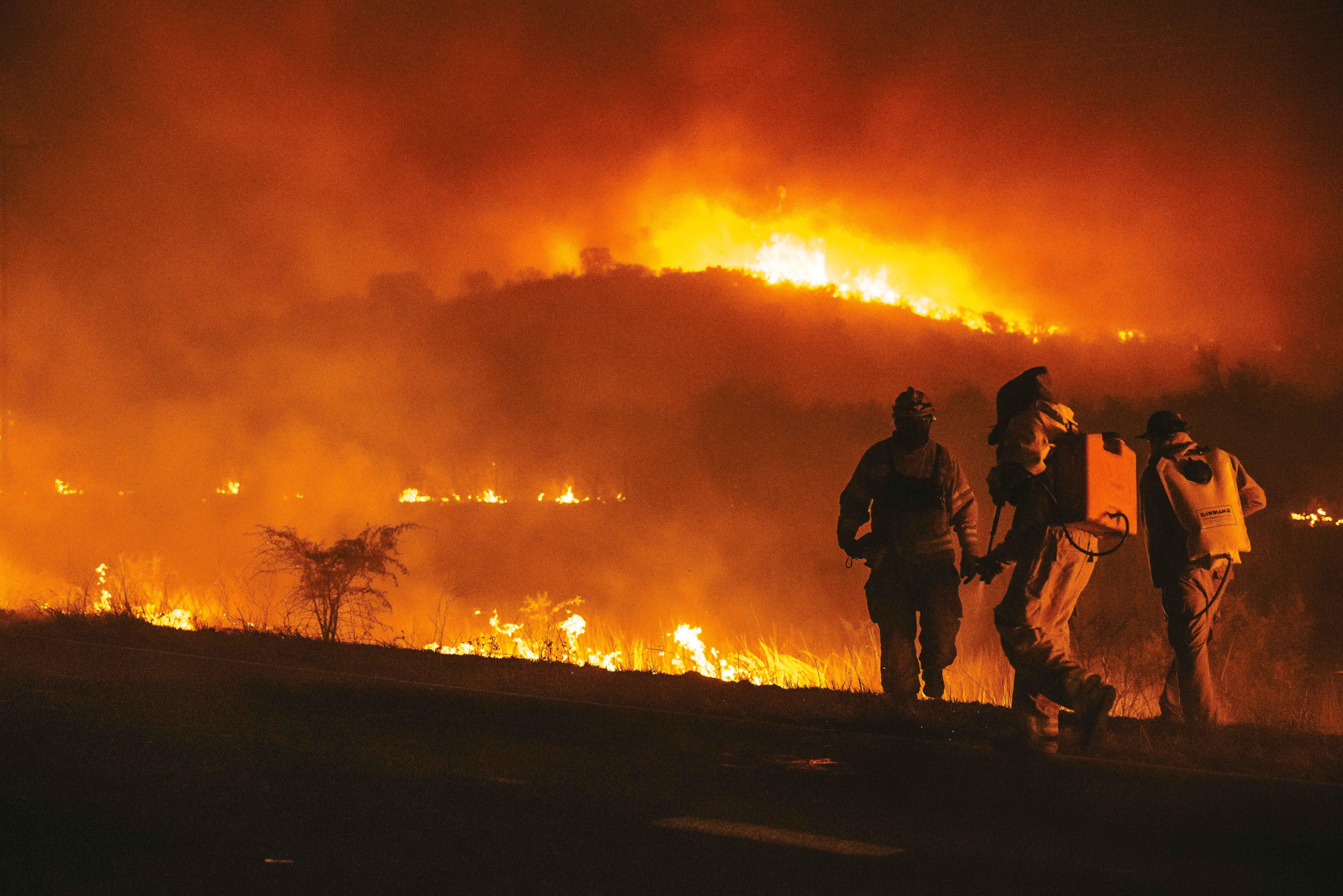 three fire fighters walking towards flaming hill