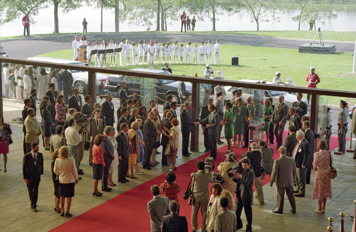 Muchas persona paradas en un salón con una alfombra roja en el medio