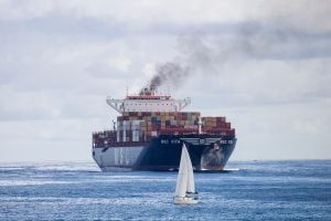 A sailboat and cargo ship navigate the ocean waters